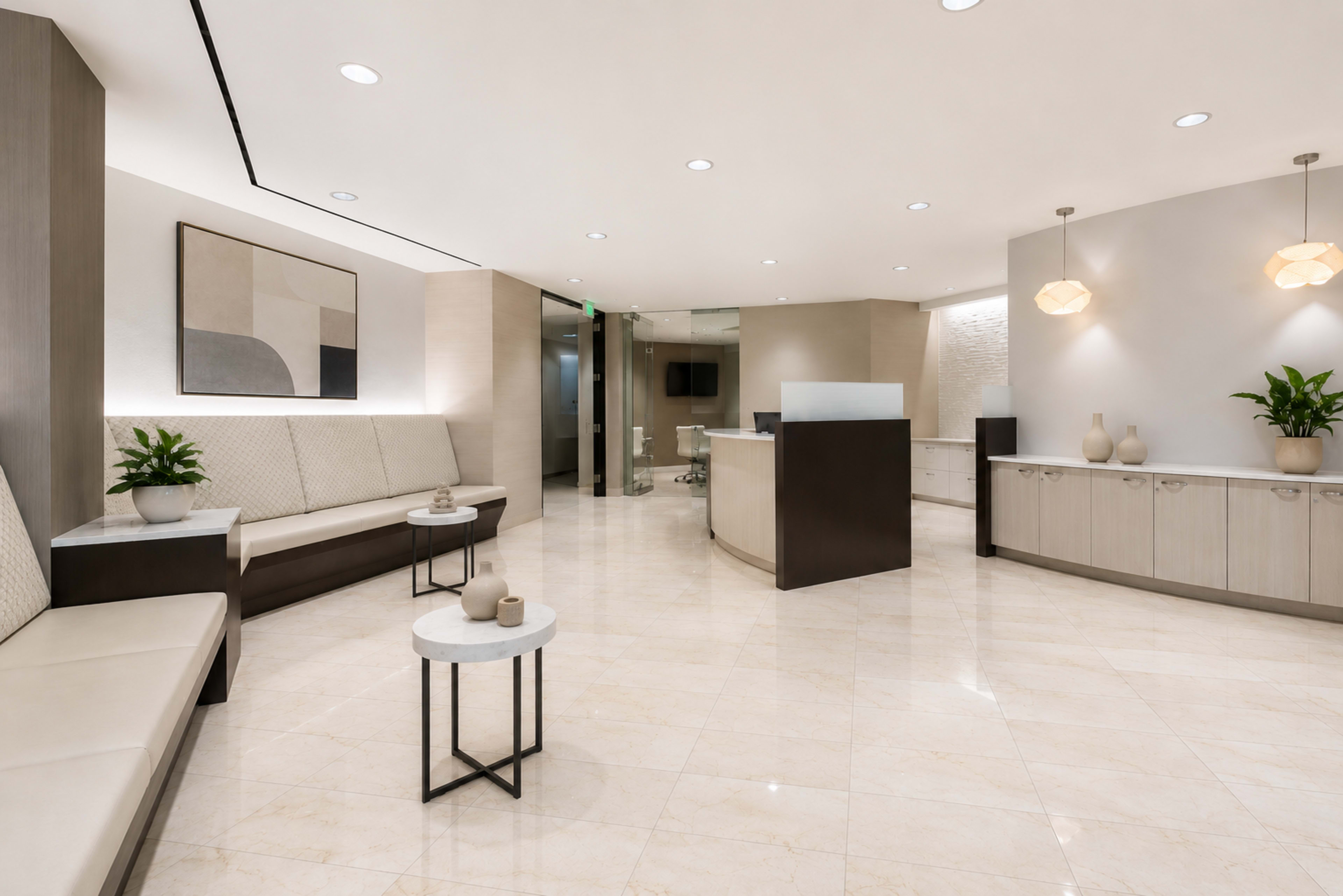 The image shows a modern reception area featuring minimalistic seating, a front desk, and decorative plants, all arranged in a bright, spacious layout.