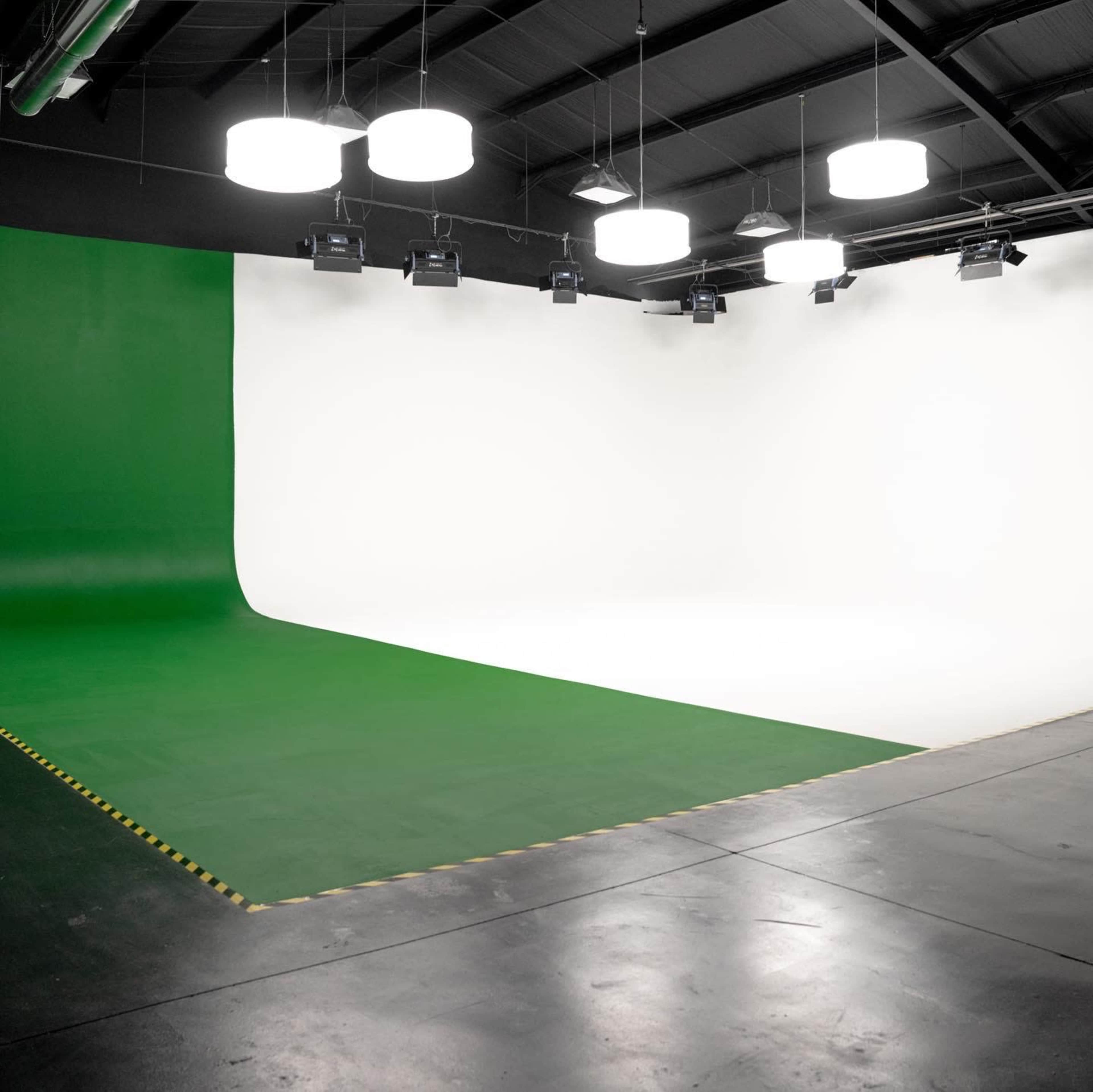 A spacious studio with a green and white backdrop, equipped with overhead lighting and projection fixtures.