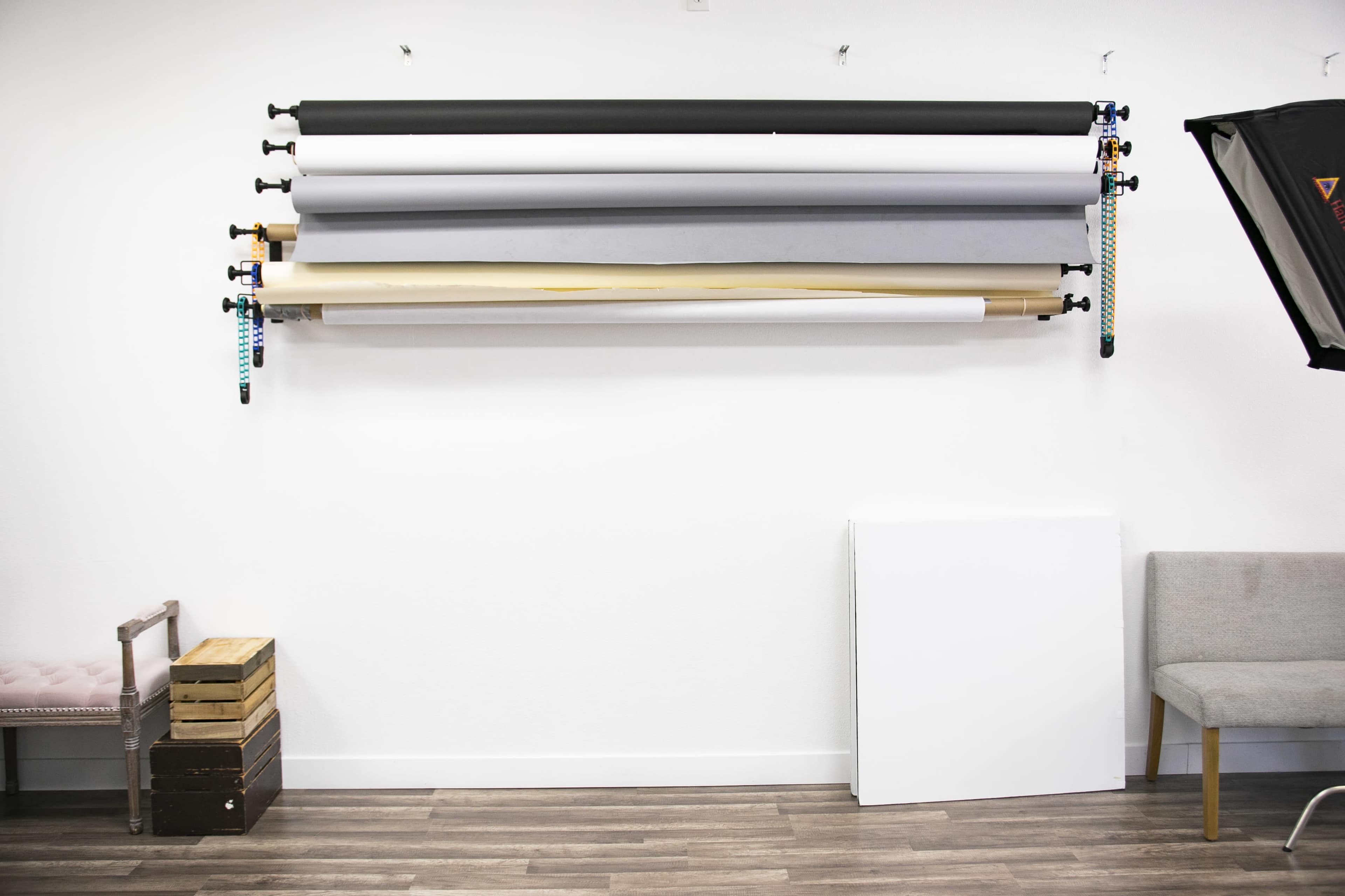 A wall displays several rolls of backdrop material above a wooden crate and a gray chair.