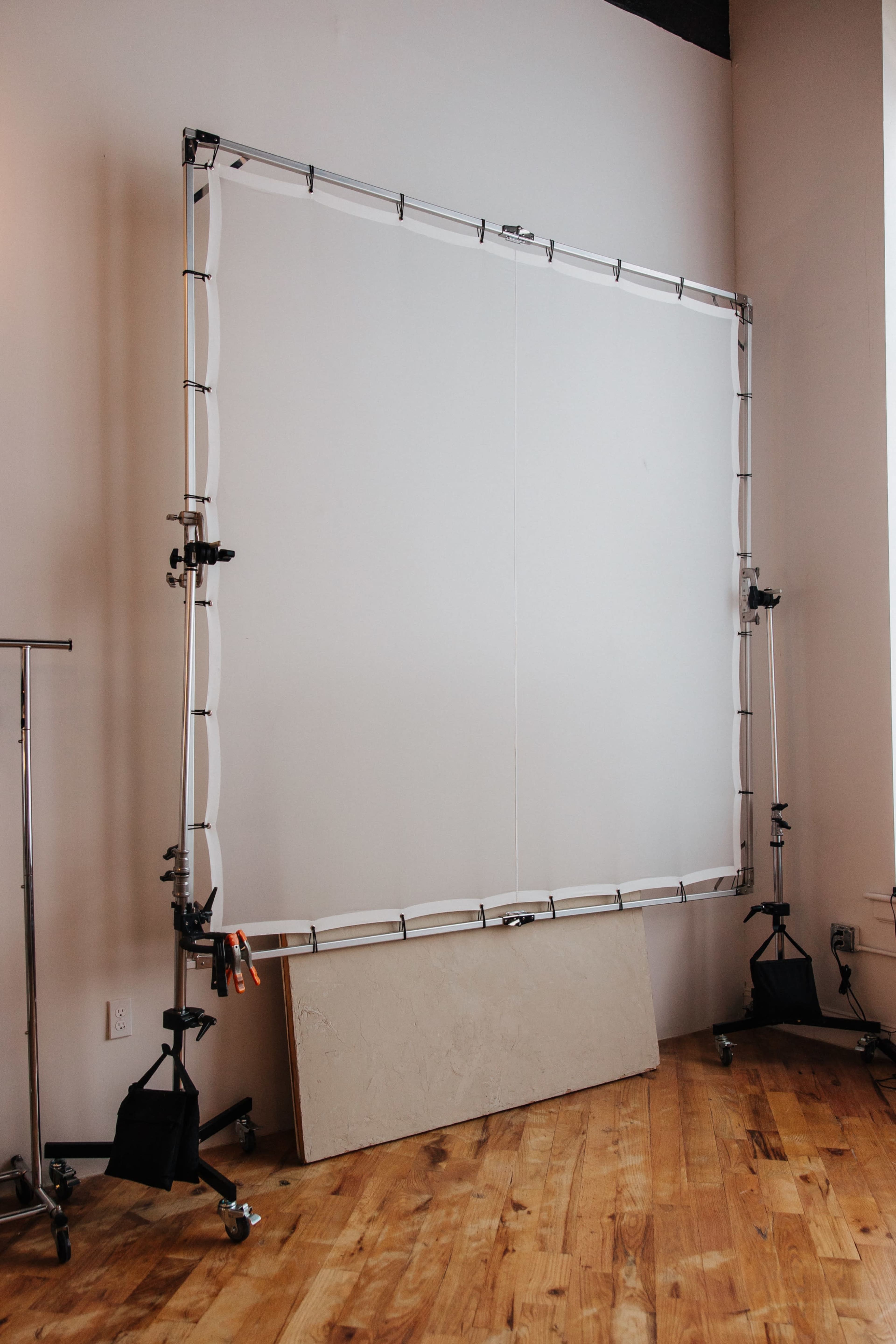 A large, adjustable photography backdrop frame stands in a studio with wooden floors.