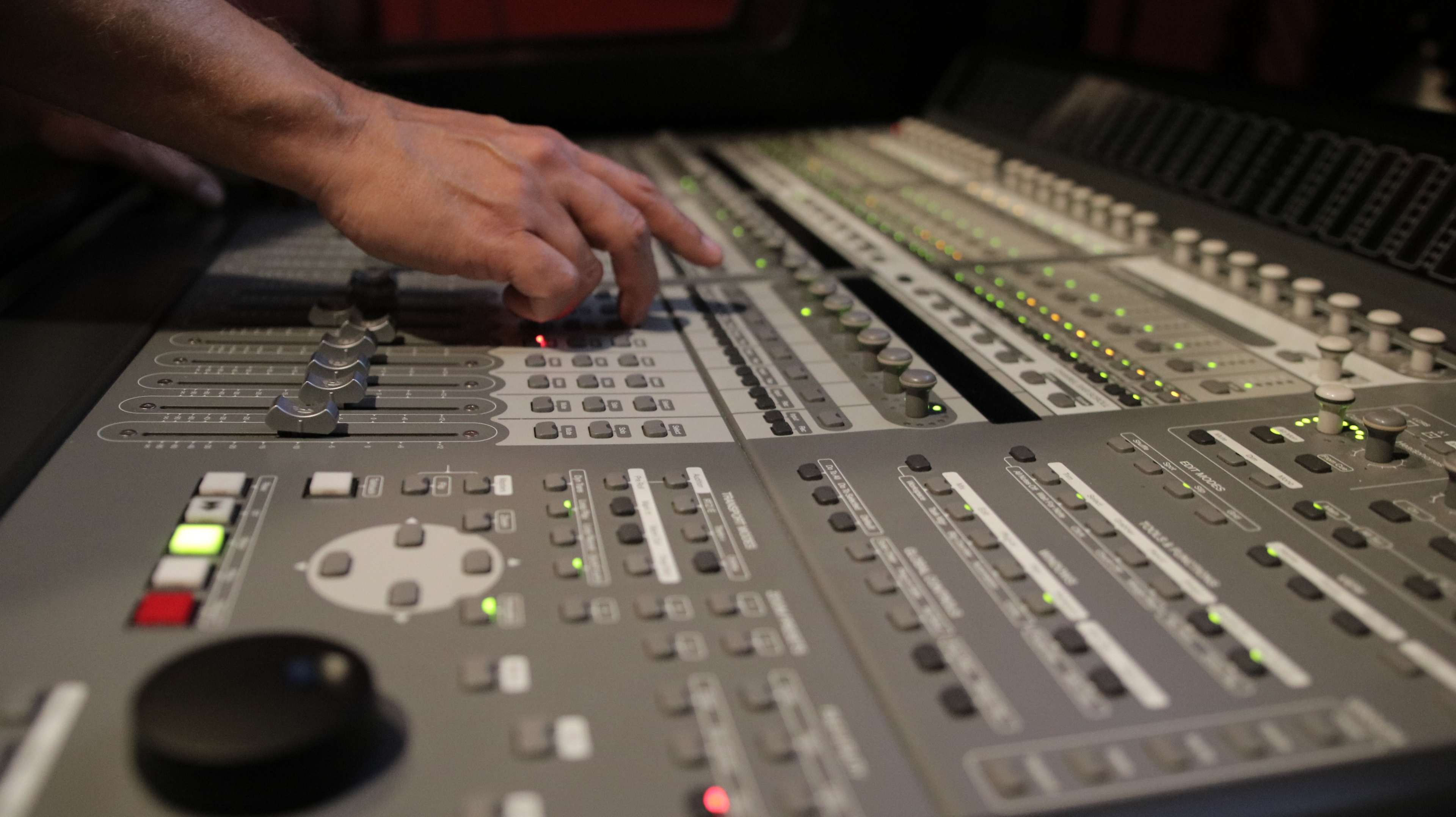 A hand adjusts the settings on a complex audio mixing console filled with knobs, sliders, and lights.