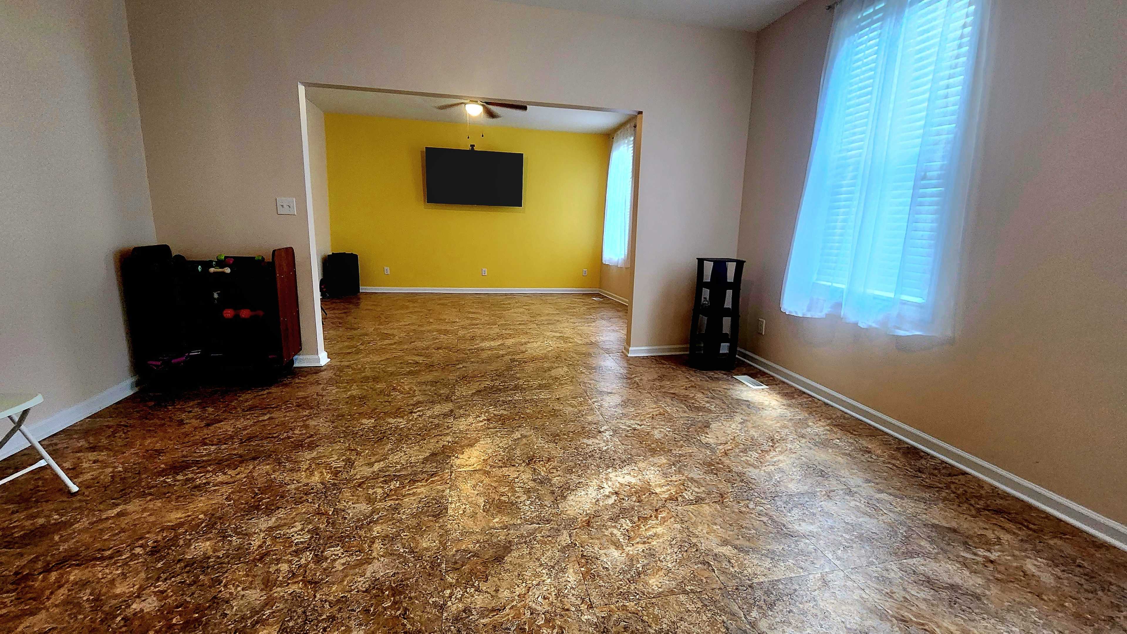 A spacious, open room with light-colored walls, a yellow accent wall, and a TV mounted on the opposite wall.