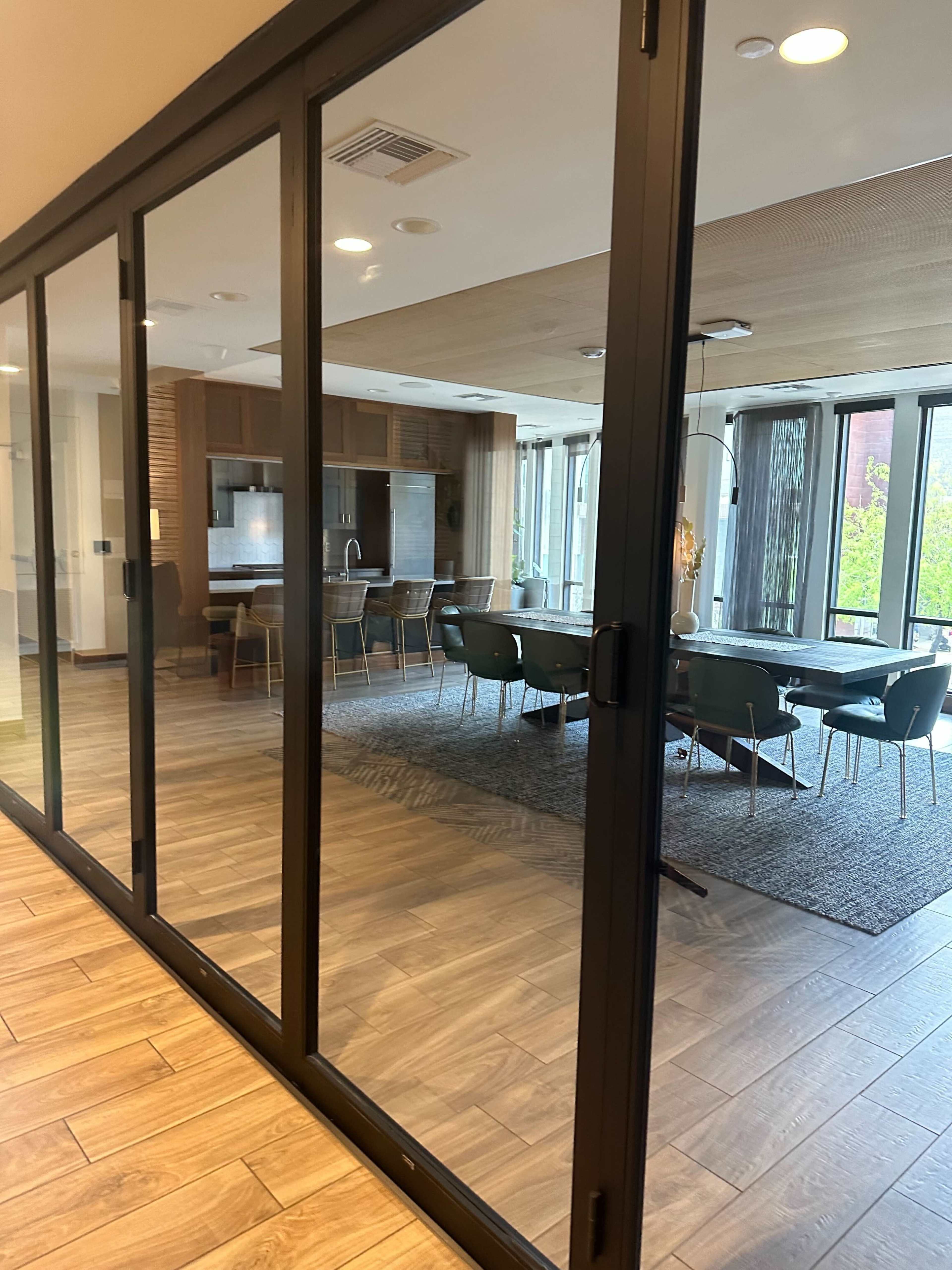 A modern kitchen and dining area are visible through large glass panels, showcasing wooden cabinetry and a dining table surrounded by chairs.