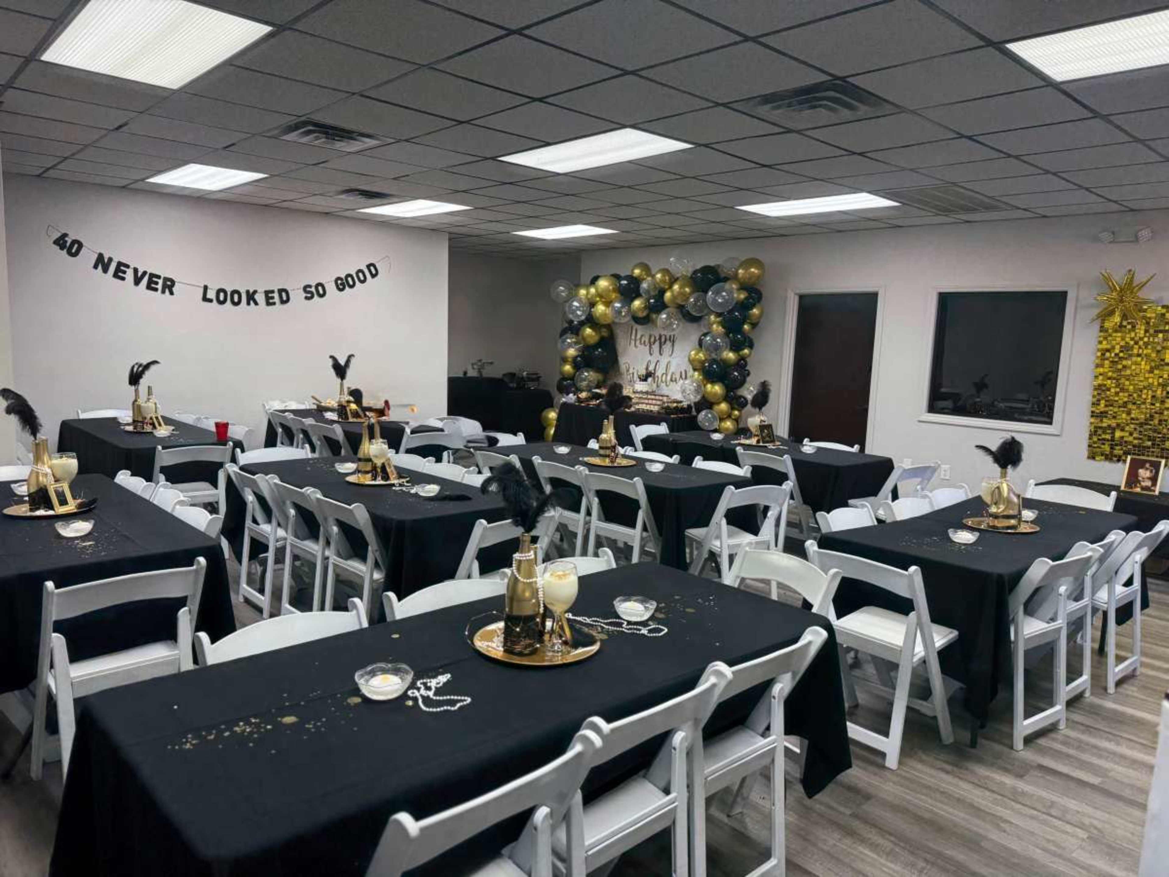 The image shows a decorated event space with black and gold table settings, featuring multiple tables and a festive display against one wall.