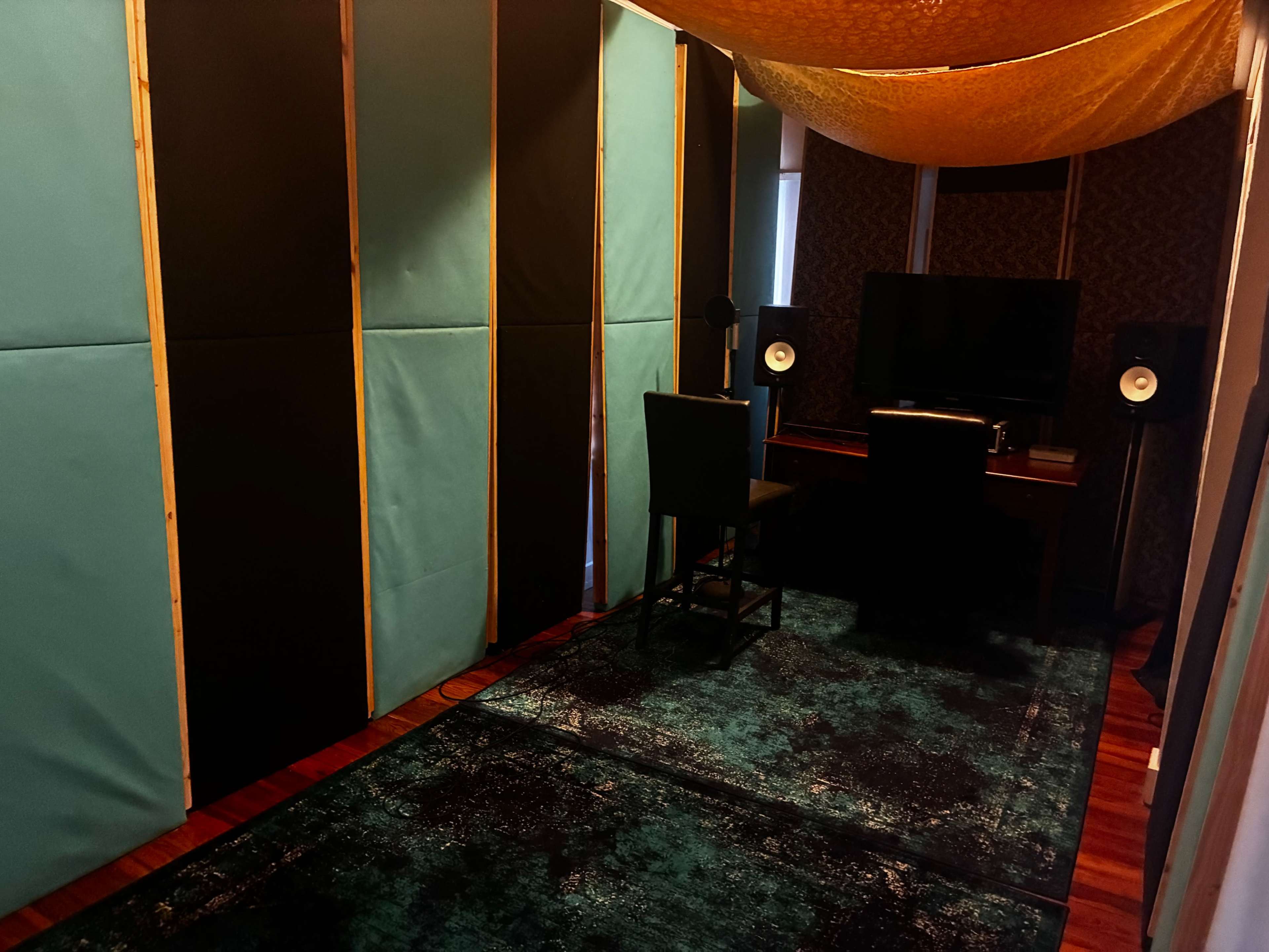 The image shows a soundproofed room with padded walls, a desk and chair, and speakers positioned near a television.