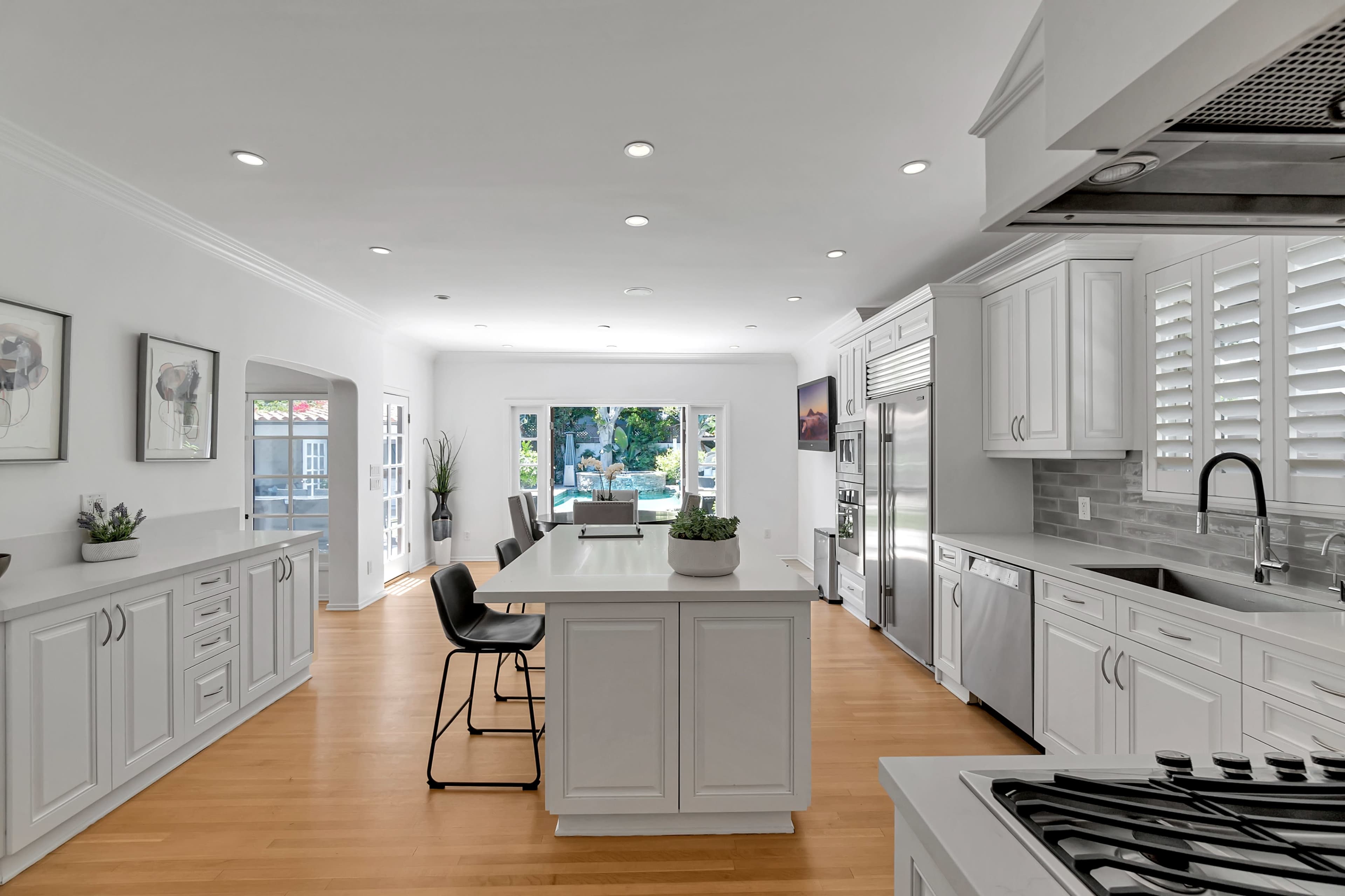 The image shows a modern kitchen with white cabinetry, a large central island, and a view of a backyard through large windows.