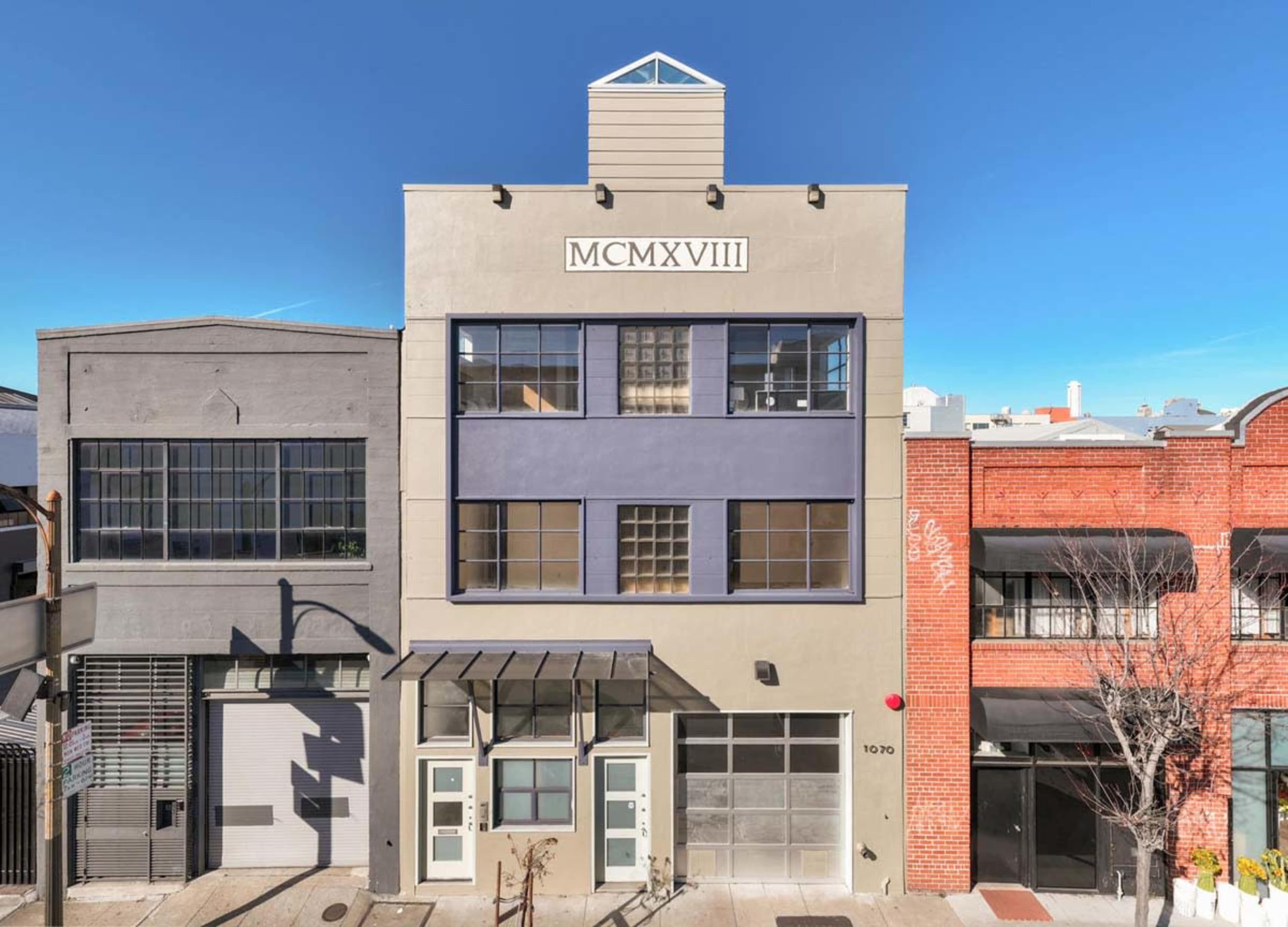 The image shows a three-story building featuring a modern facade, with large windows and the year "MCMXVIII" displayed prominently above the entrance.