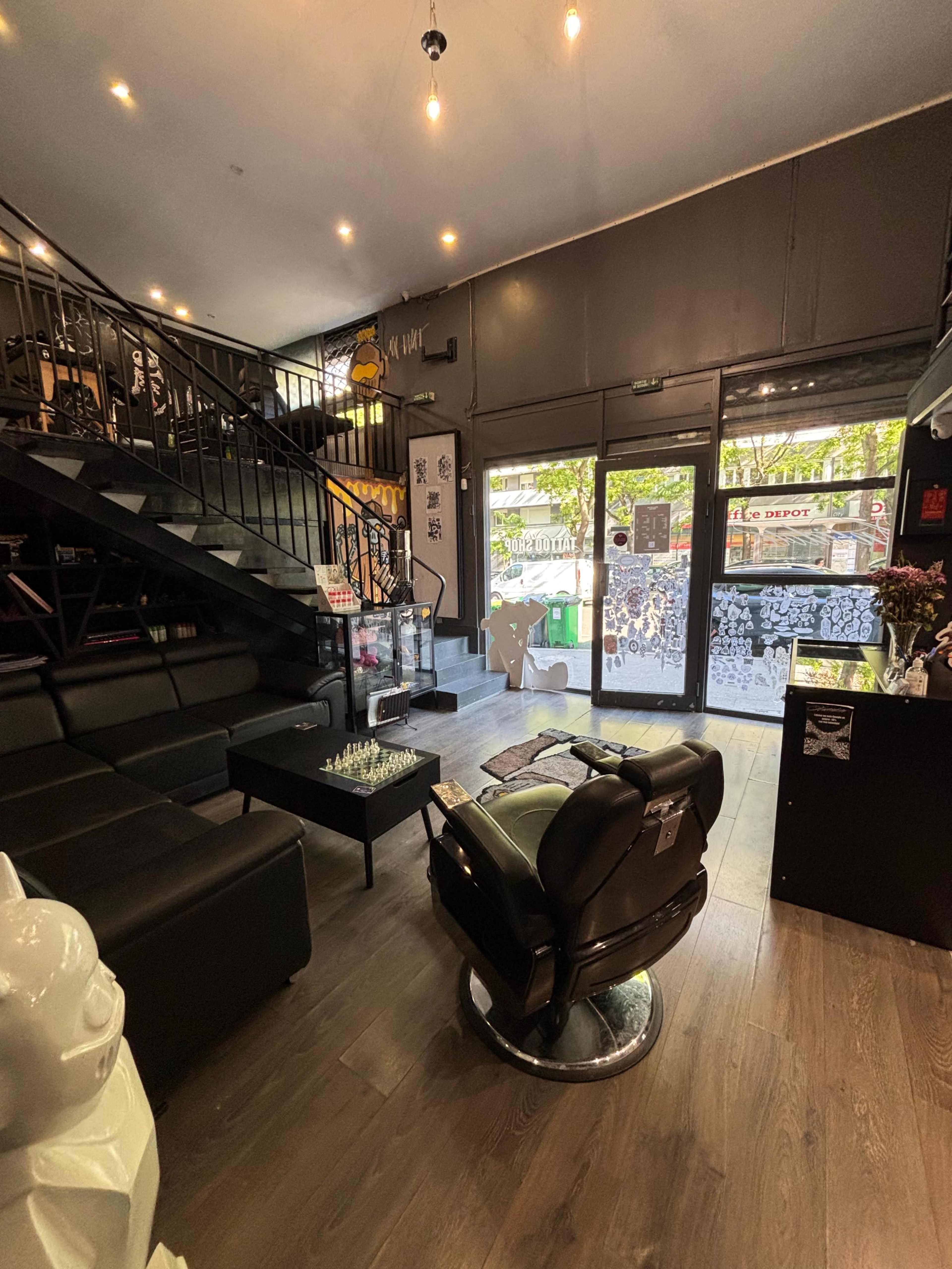 The image shows a modern barbershop interior featuring a black leather barber chair, a staircase, and large windows with views of the outside.