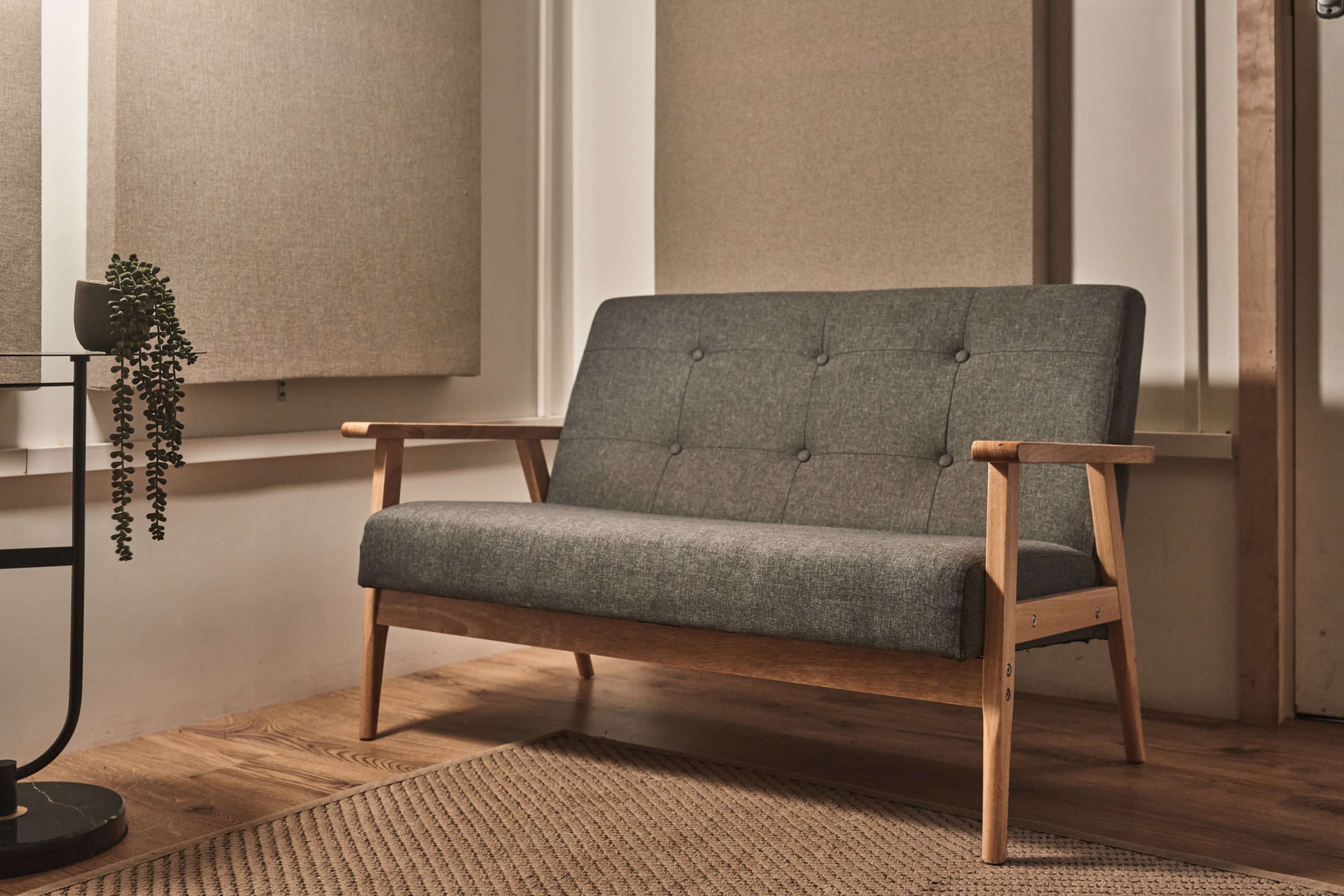 A gray upholstered sofa with wooden arms is positioned on a wooden floor next to two textured wall panels.