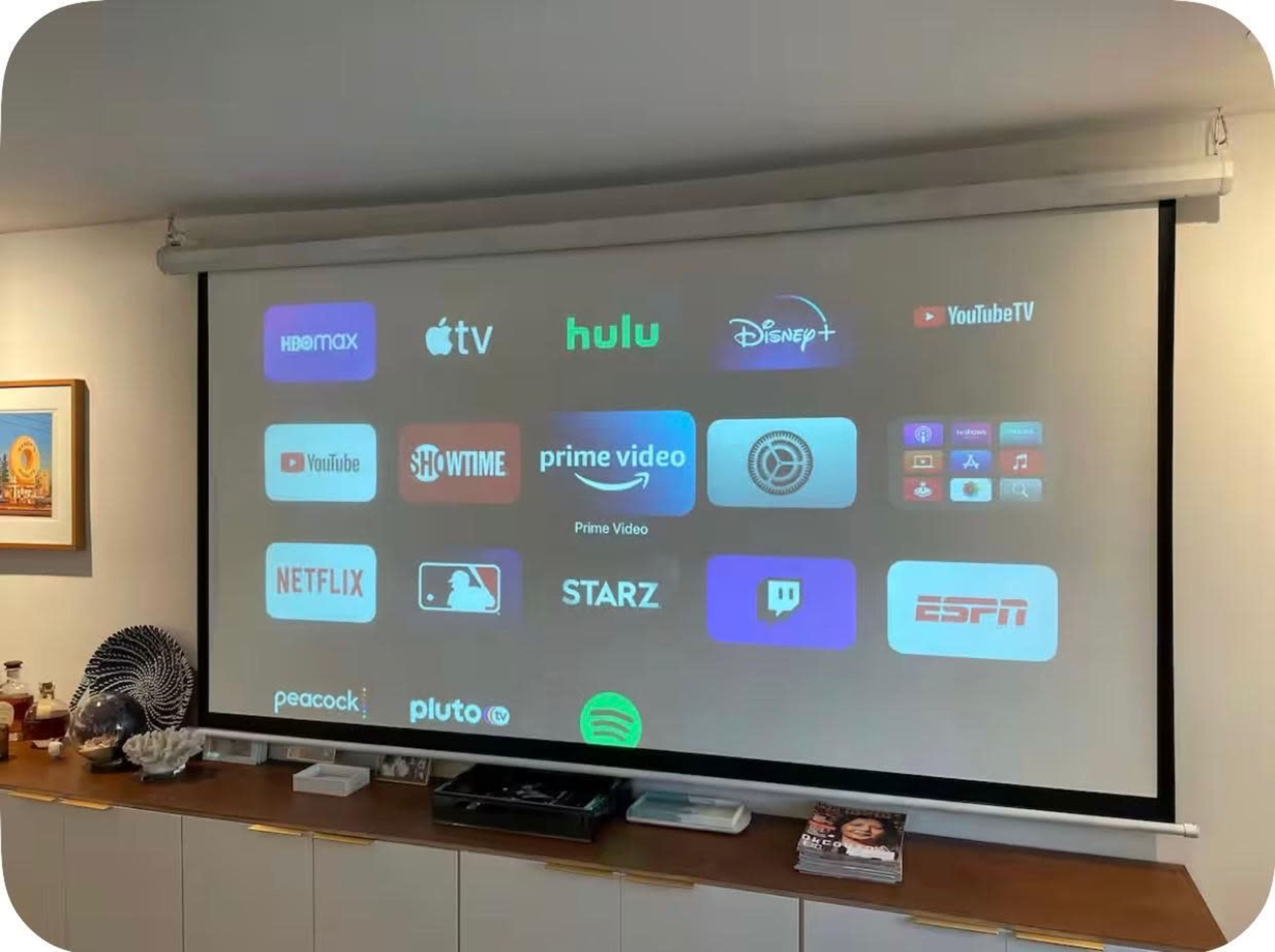 The image displays a projector screen featuring various streaming service logos, including HBO Max, Apple TV, Hulu, Disney+, and Netflix.