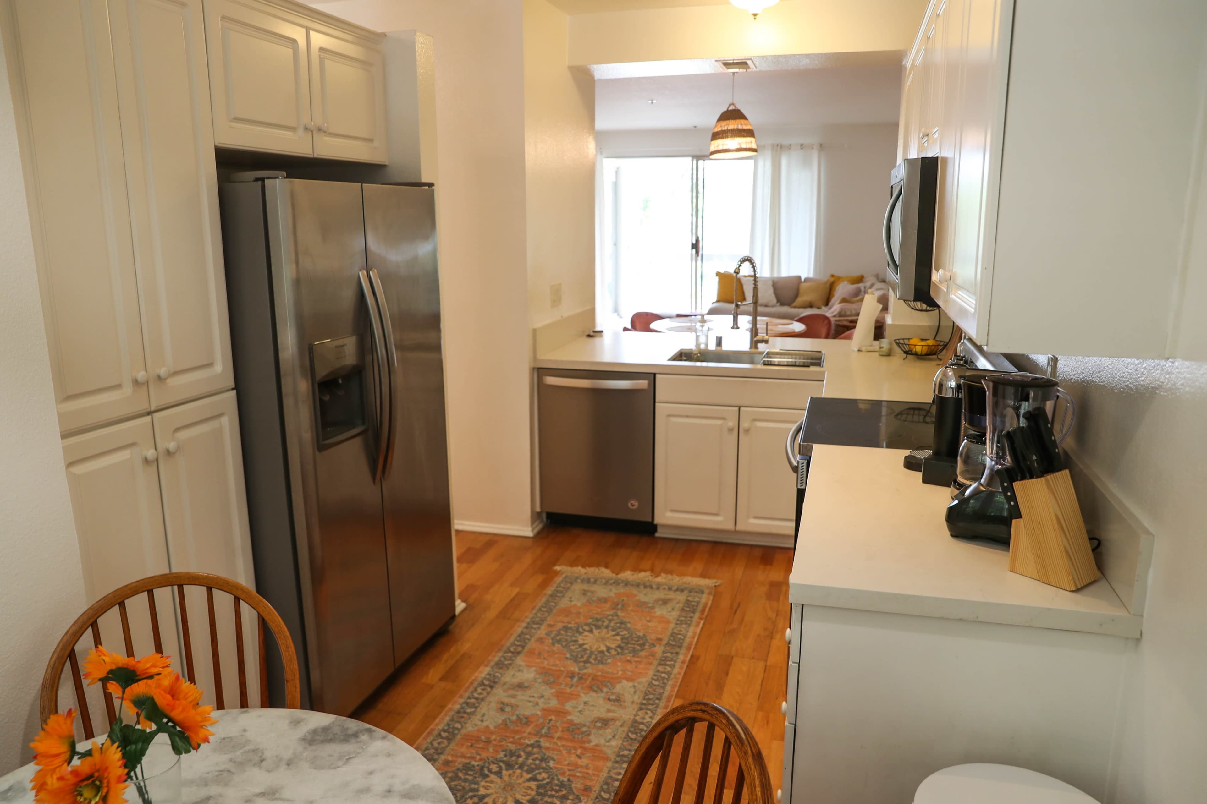 A modern kitchen with stainless steel appliances, white cabinetry, and a small dining table adorned with flowers.