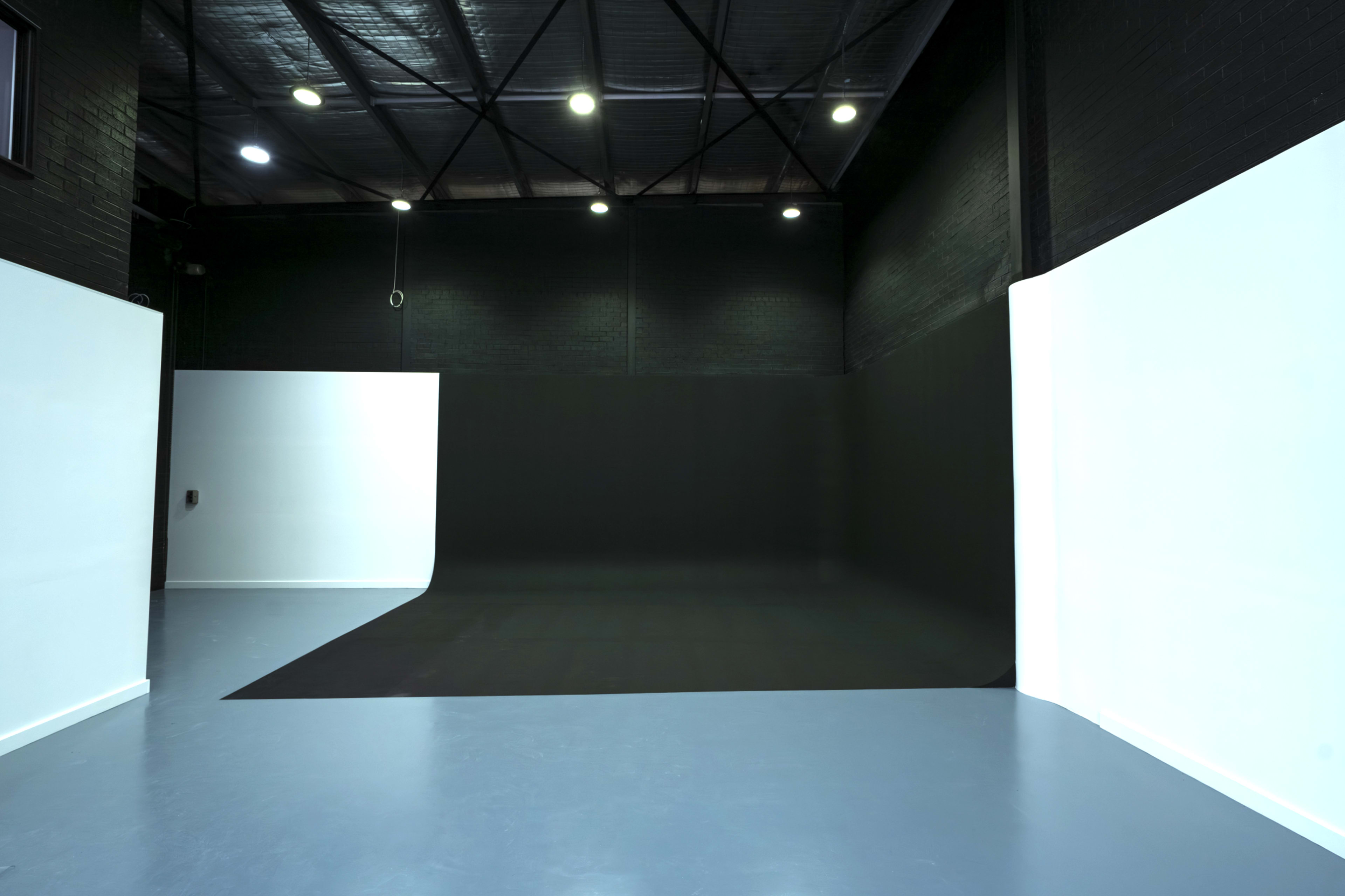 The image shows a spacious studio with a black backdrop on one side and white walls combined with a light blue floor.