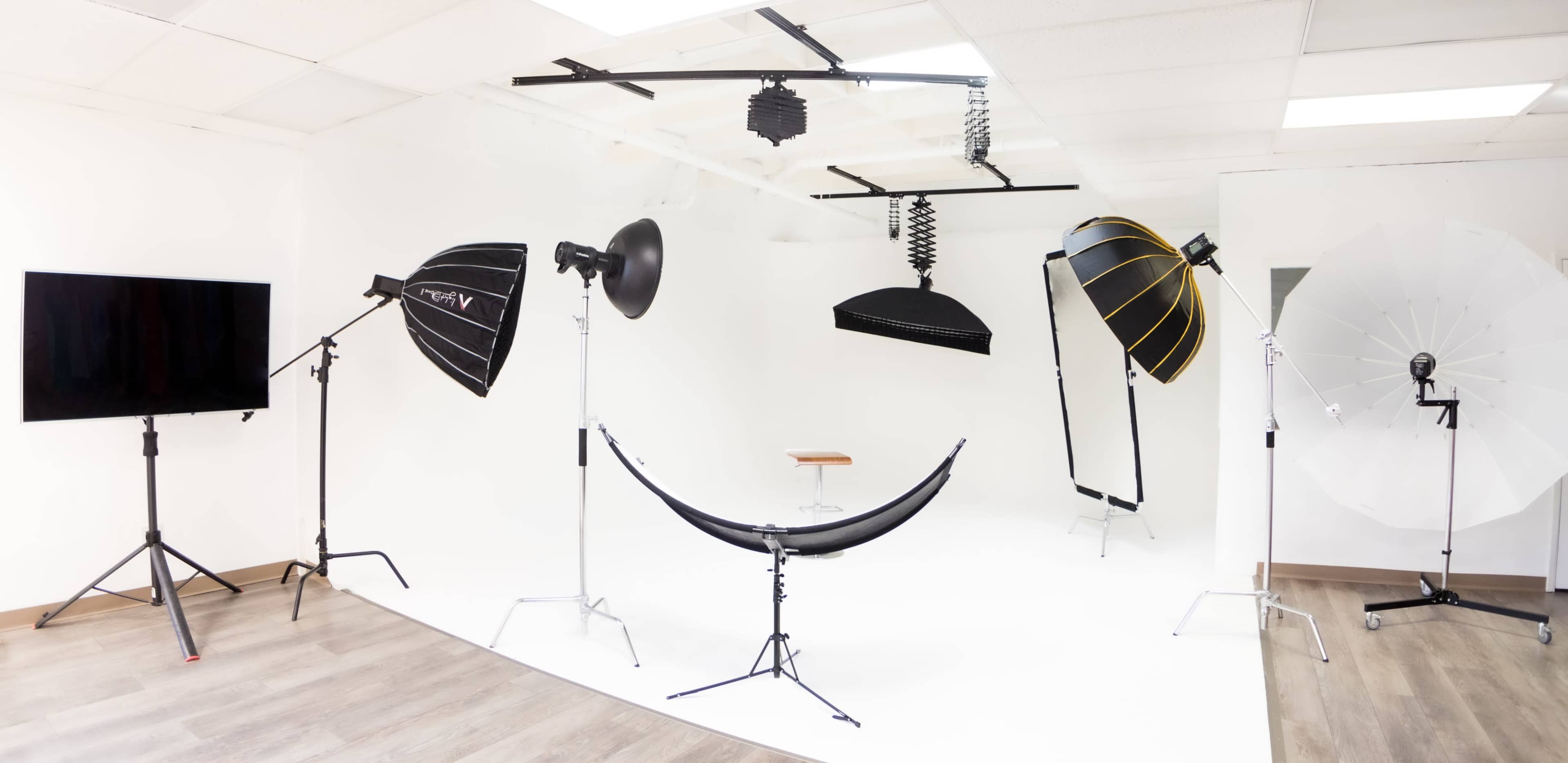 A photography studio equipped with multiple light sources, softboxes, and a wooden stool on a white backdrop.
