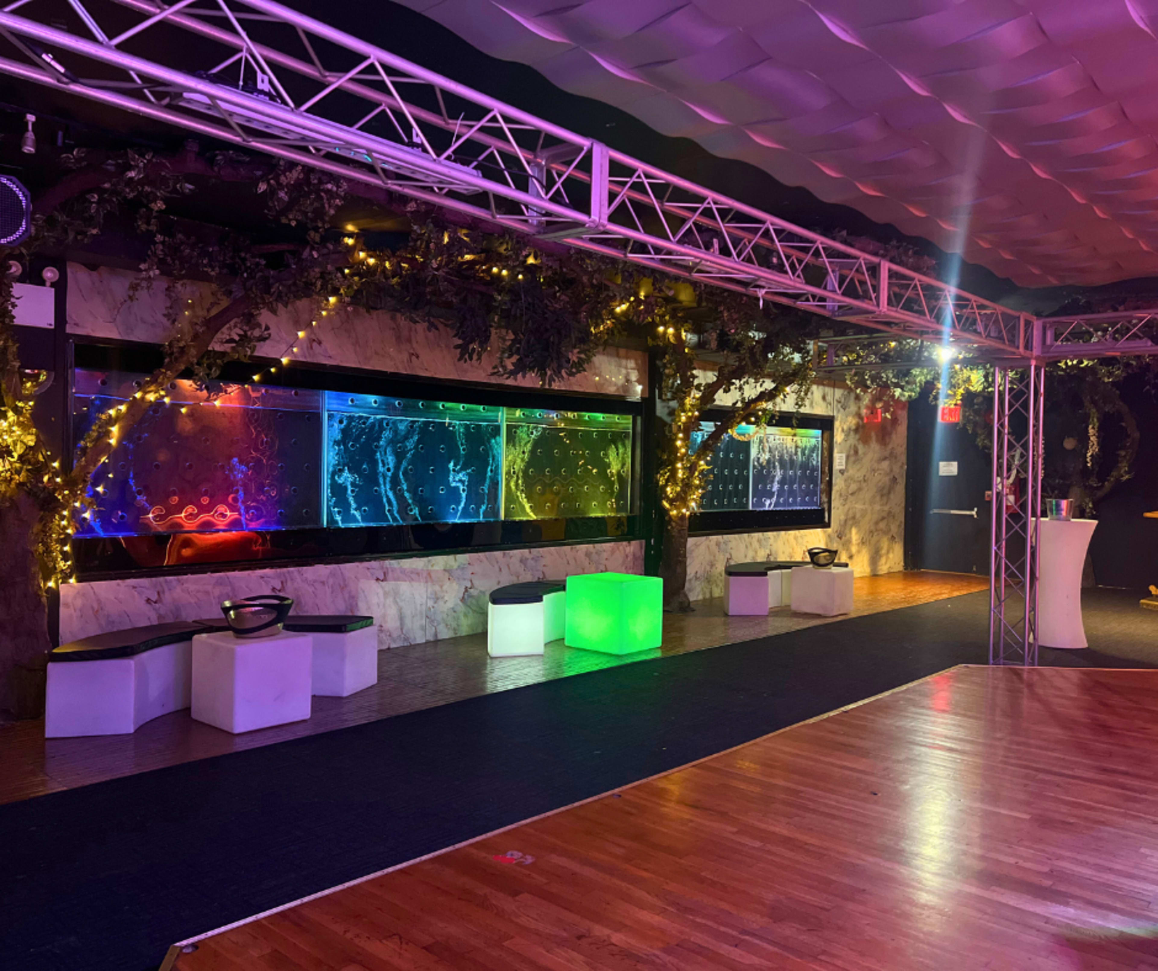 The image shows a dimly lit event space featuring colorful wall-mounted displays with water effects, surrounded by ambient lighting and modern seating arrangements.