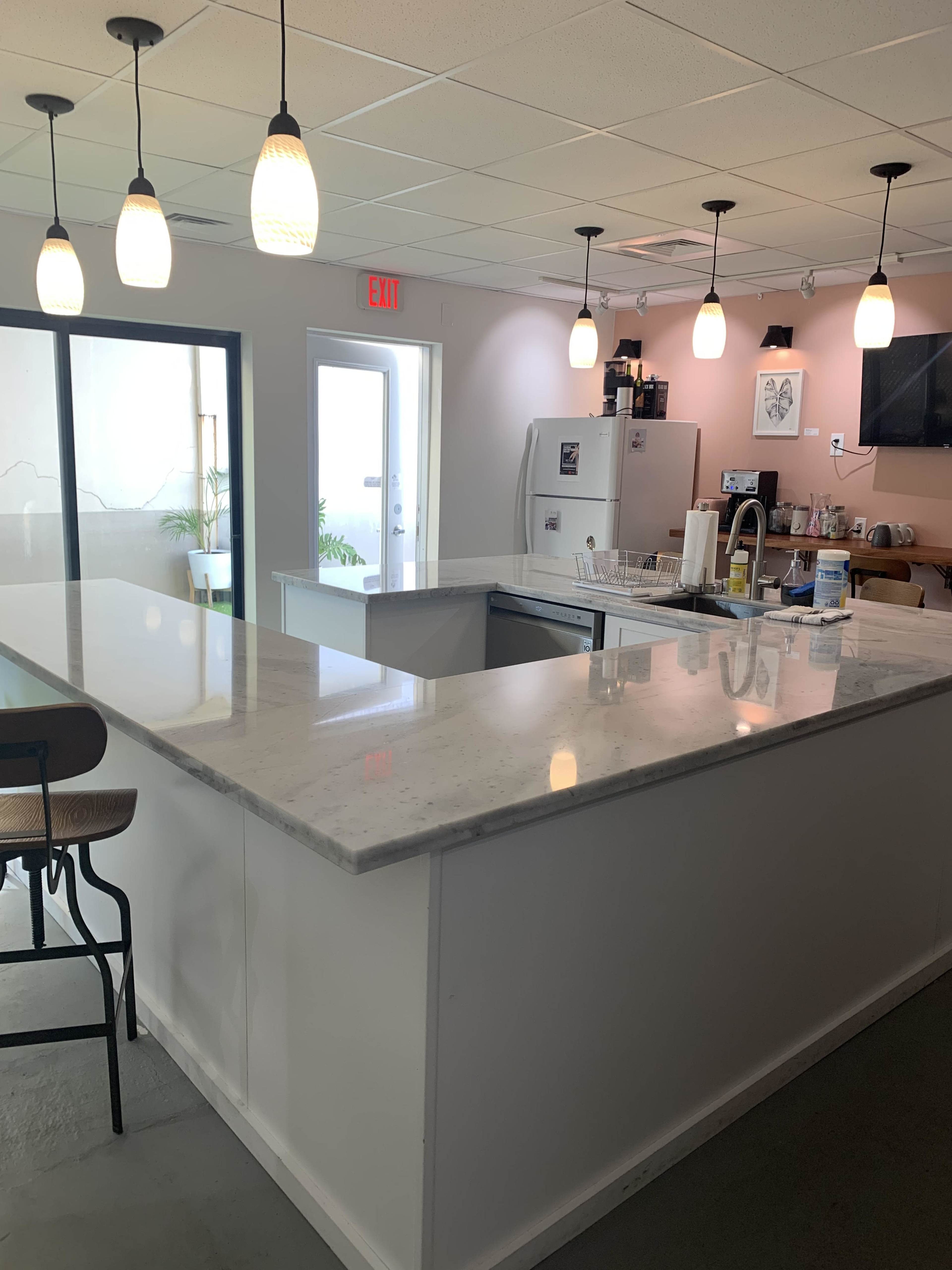 A modern kitchen features a large white countertop with pendant lights overhead and a view of a door leading outside.