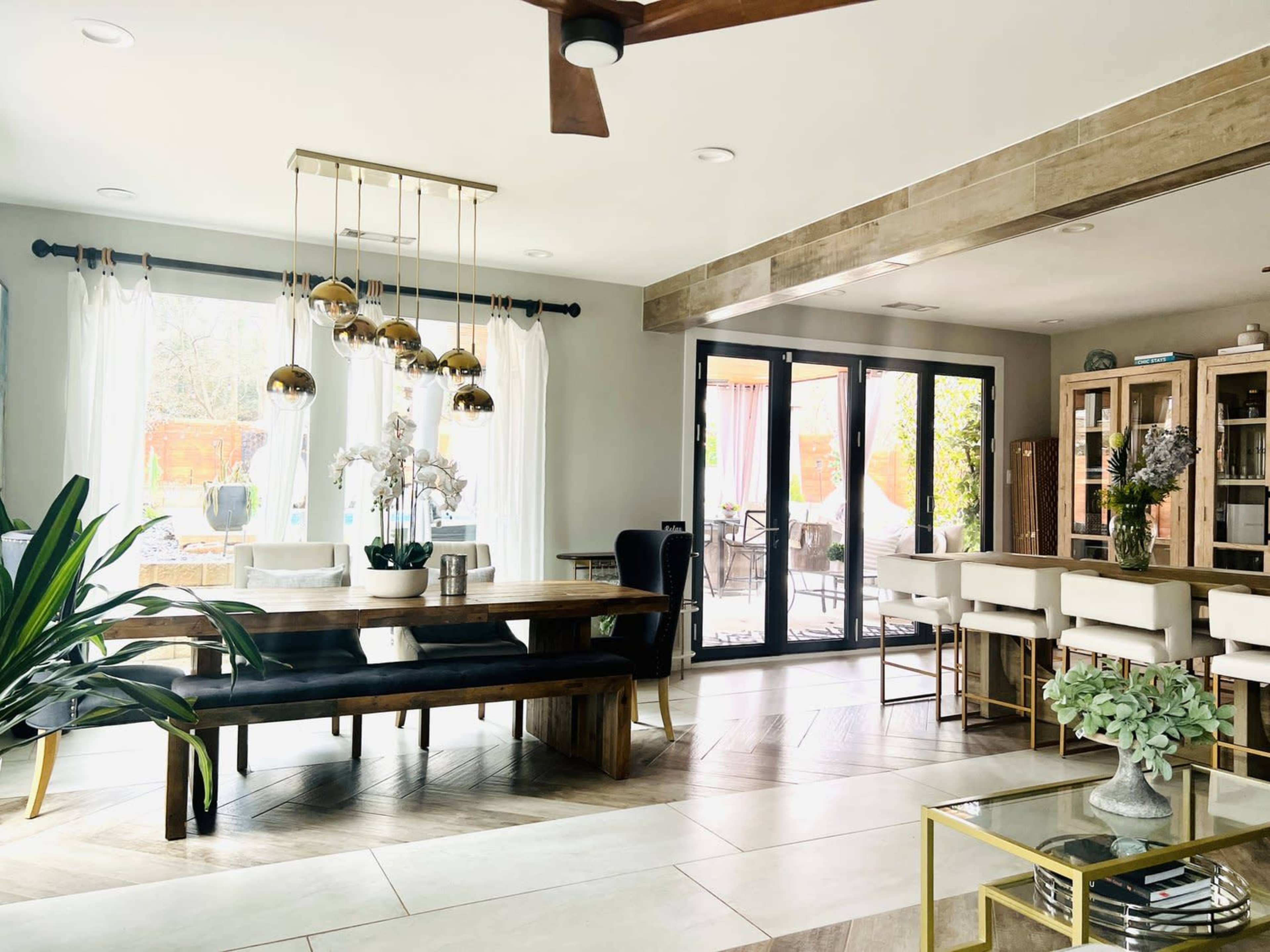 A modern dining area with a long table, elegant pendant lights, and large sliding glass doors leading to an outdoor space.