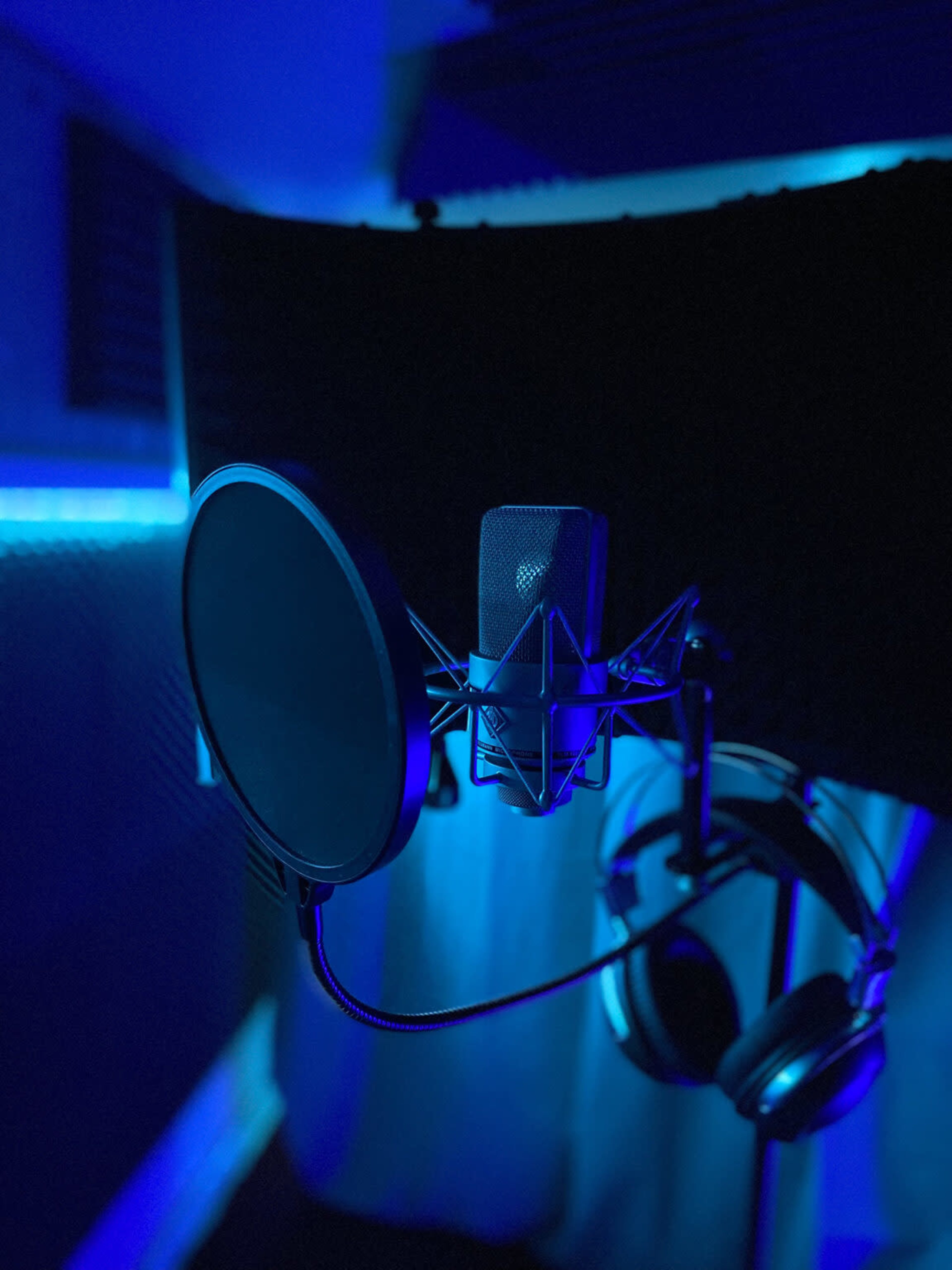 A microphone with a pop filter and headphones is set up in a dimly lit recording studio.