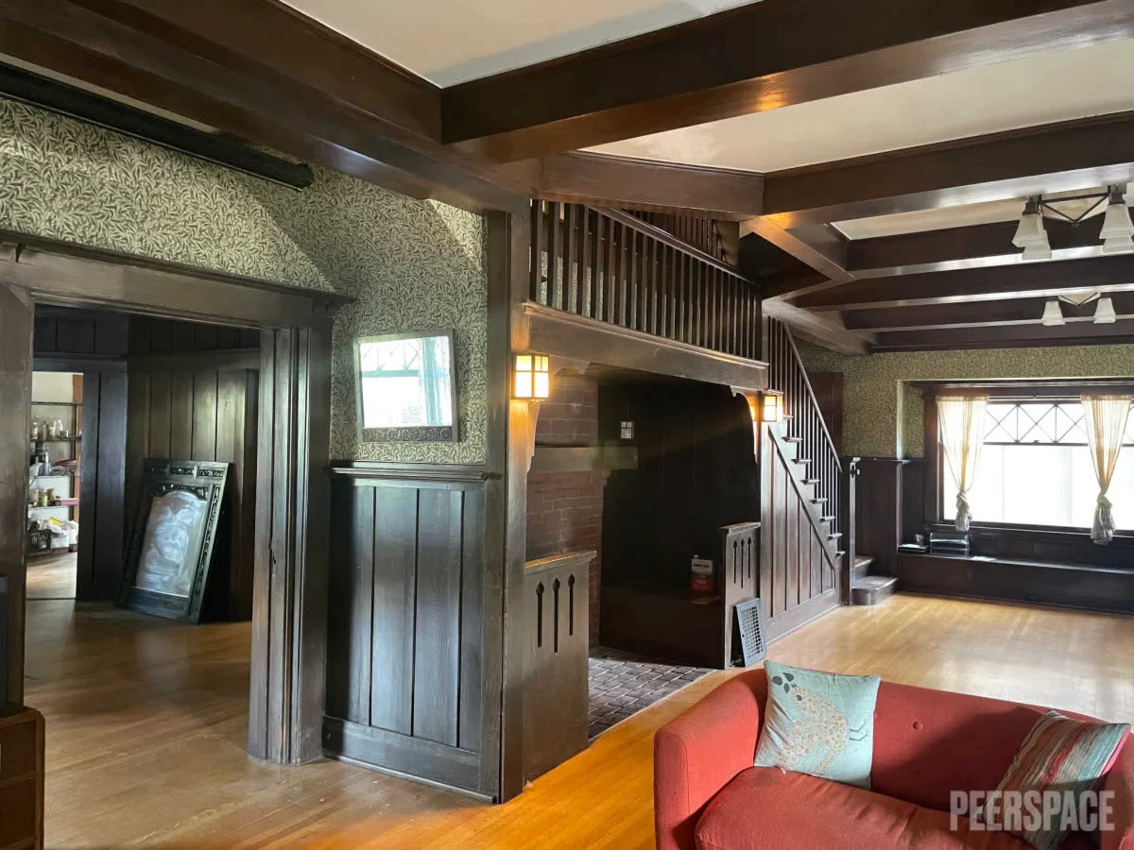 A spacious, multi-level interior of a home featuring dark wood paneling, decorative wallpaper, and a staircase leading to the upper level.