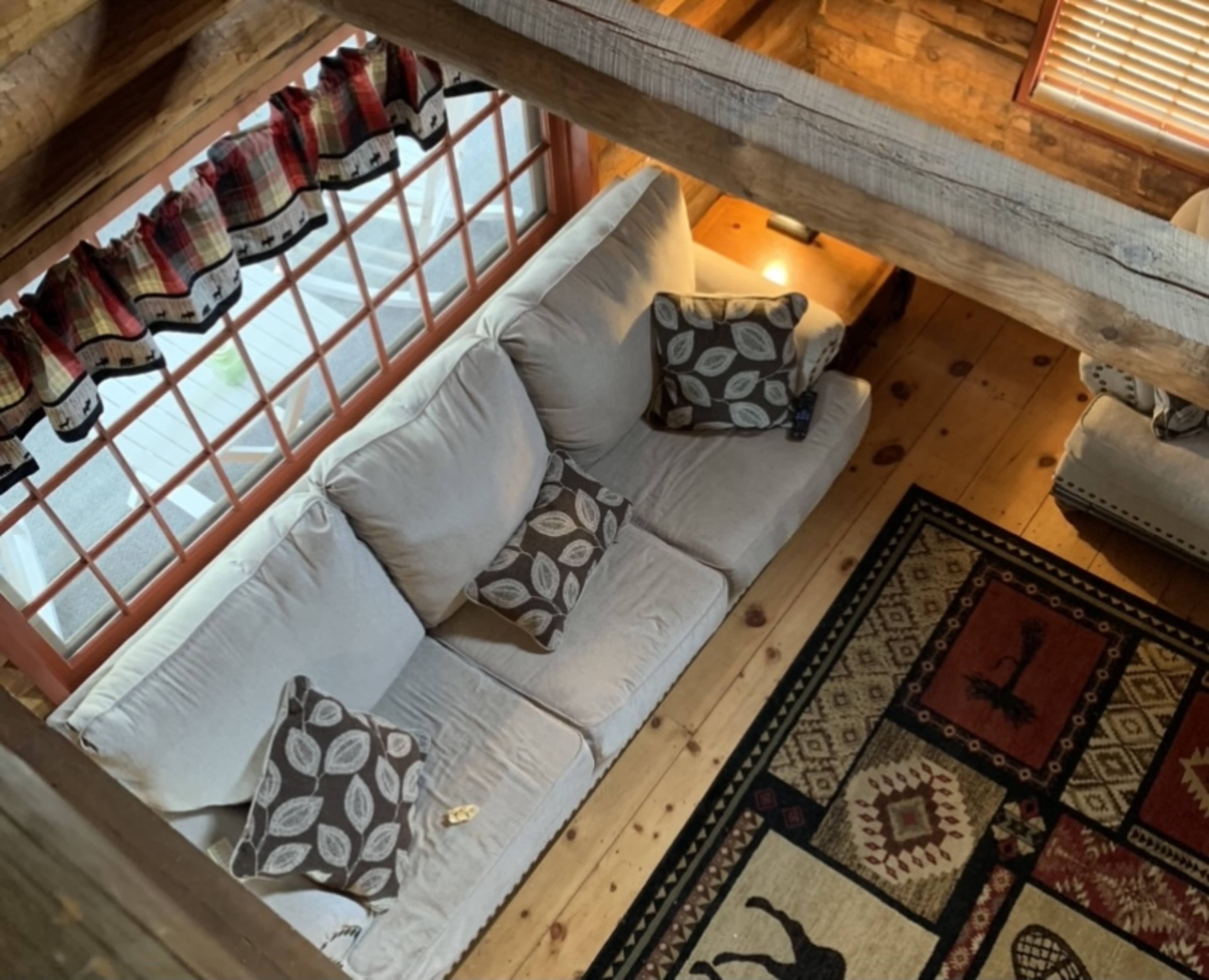 An overhead view of a cozy living room with a beige couch adorned with patterned pillows, situated on a wooden floor and surrounded by a patterned rug.