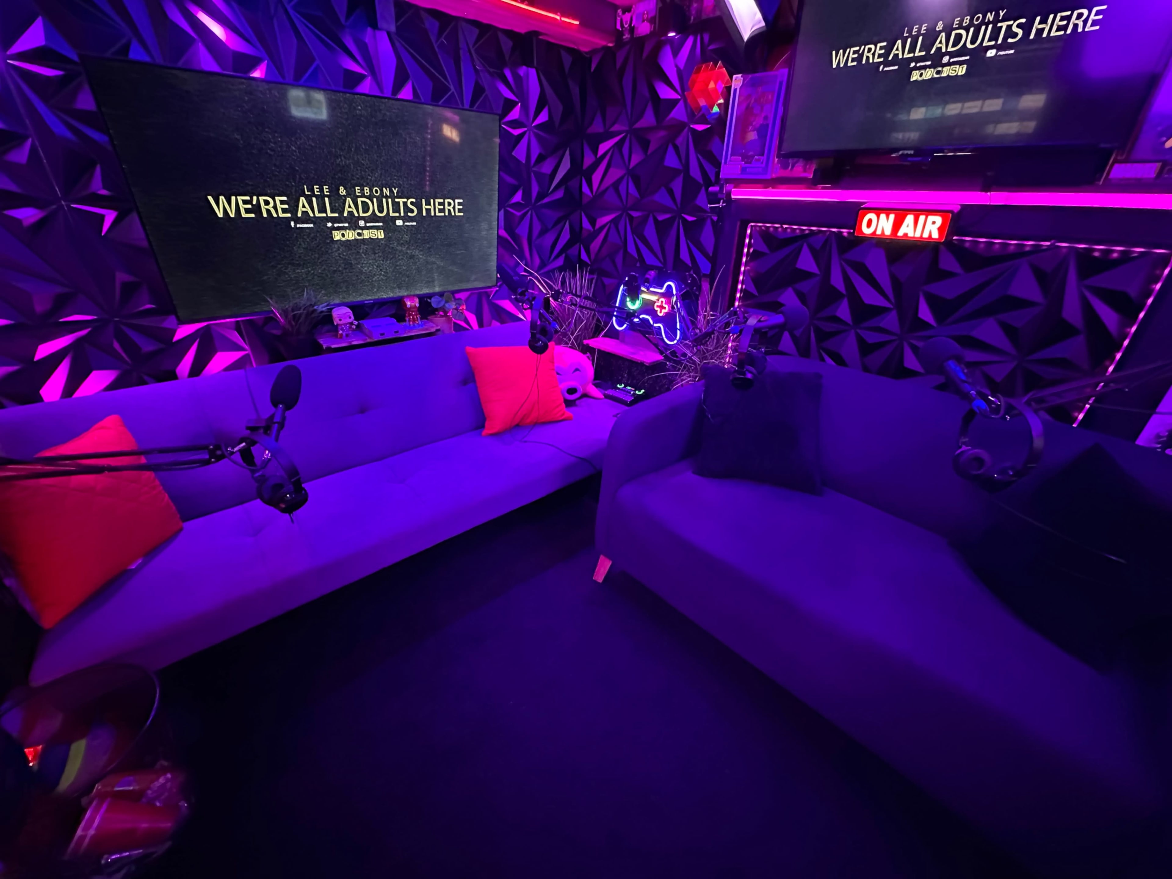 The image shows a modern recording studio with purple couches, microphones, neon lighting, and screens displaying "WE'RE ALL ADULTS HERE."