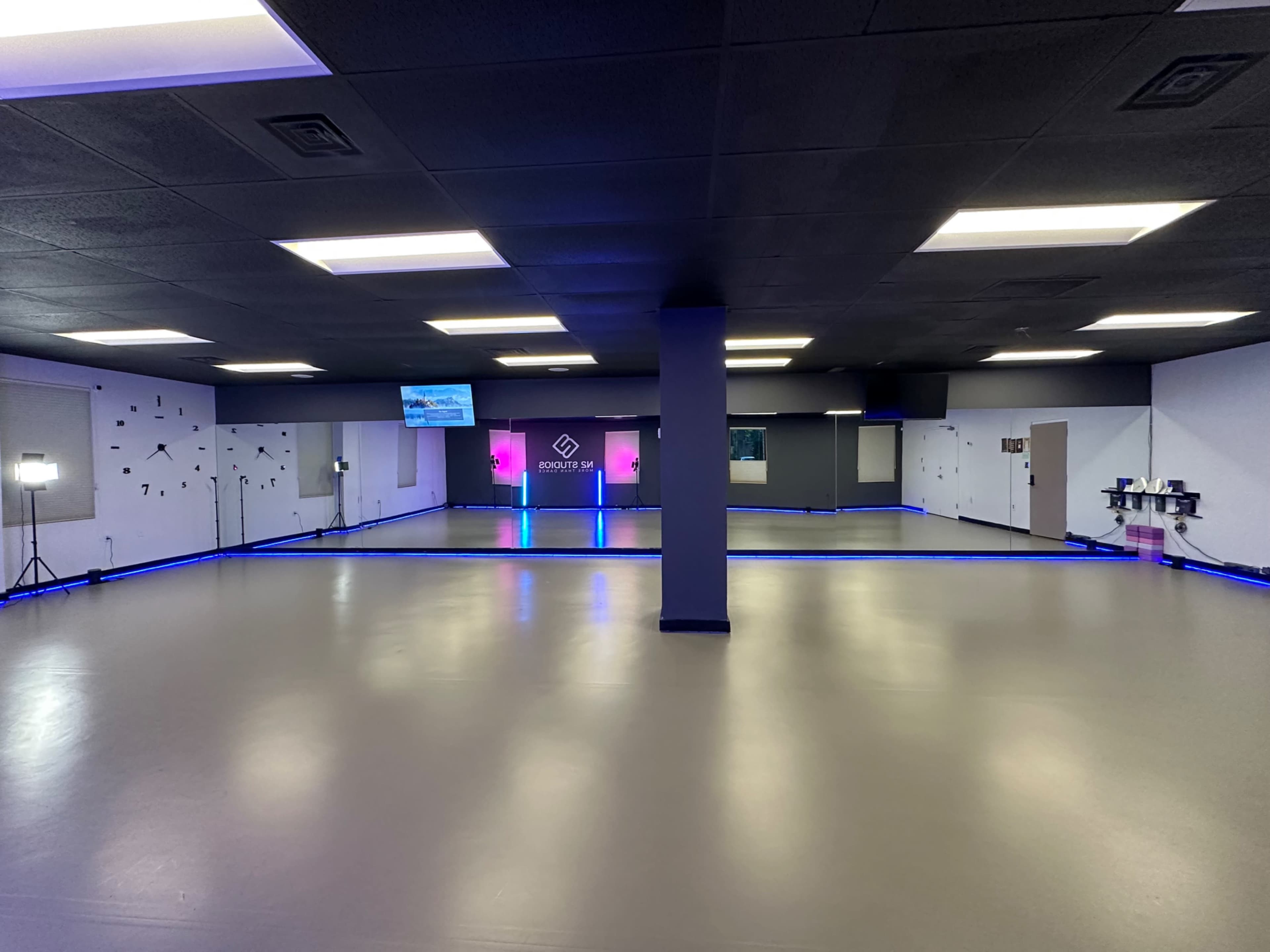 A spacious, empty room with a dark ceiling and walls lined with blue LED lighting, featuring a reception area at the far end with screens and lighting.