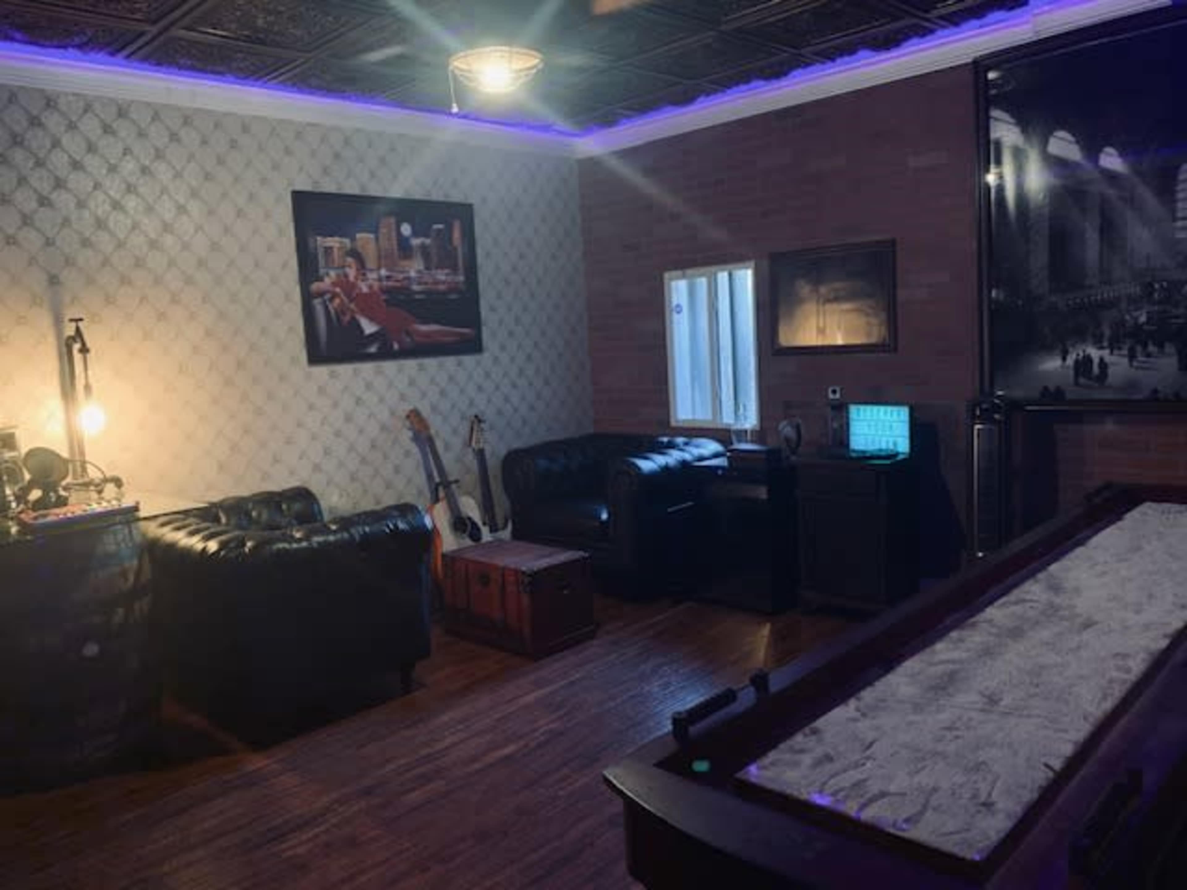 The image depicts a cozy room with leather couches, a window, a wooden floor, and a pool table, complemented by wall art and ambient lighting.
