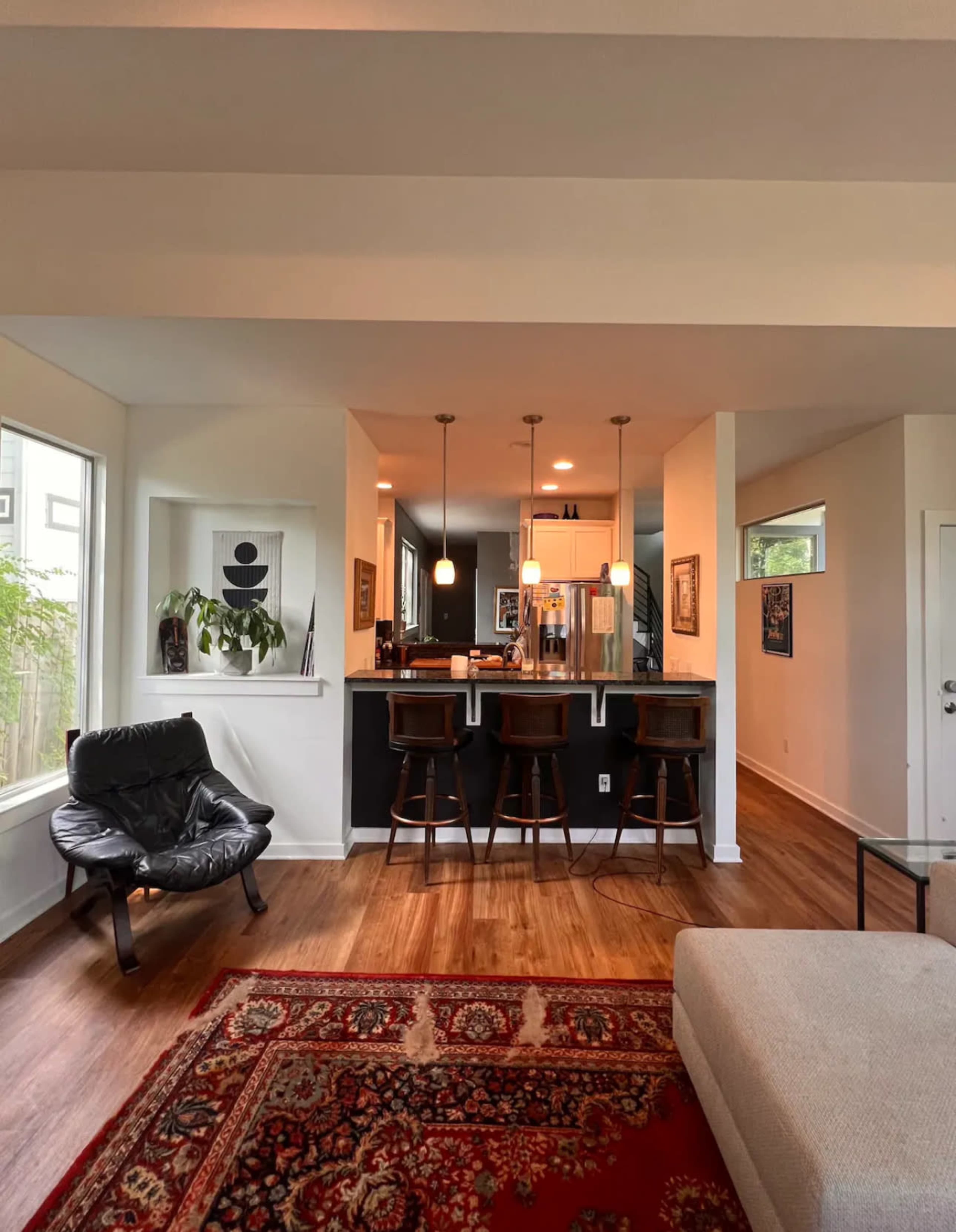 A modern open-concept living area with a seating area, a rug, and a kitchen bar with three stools.