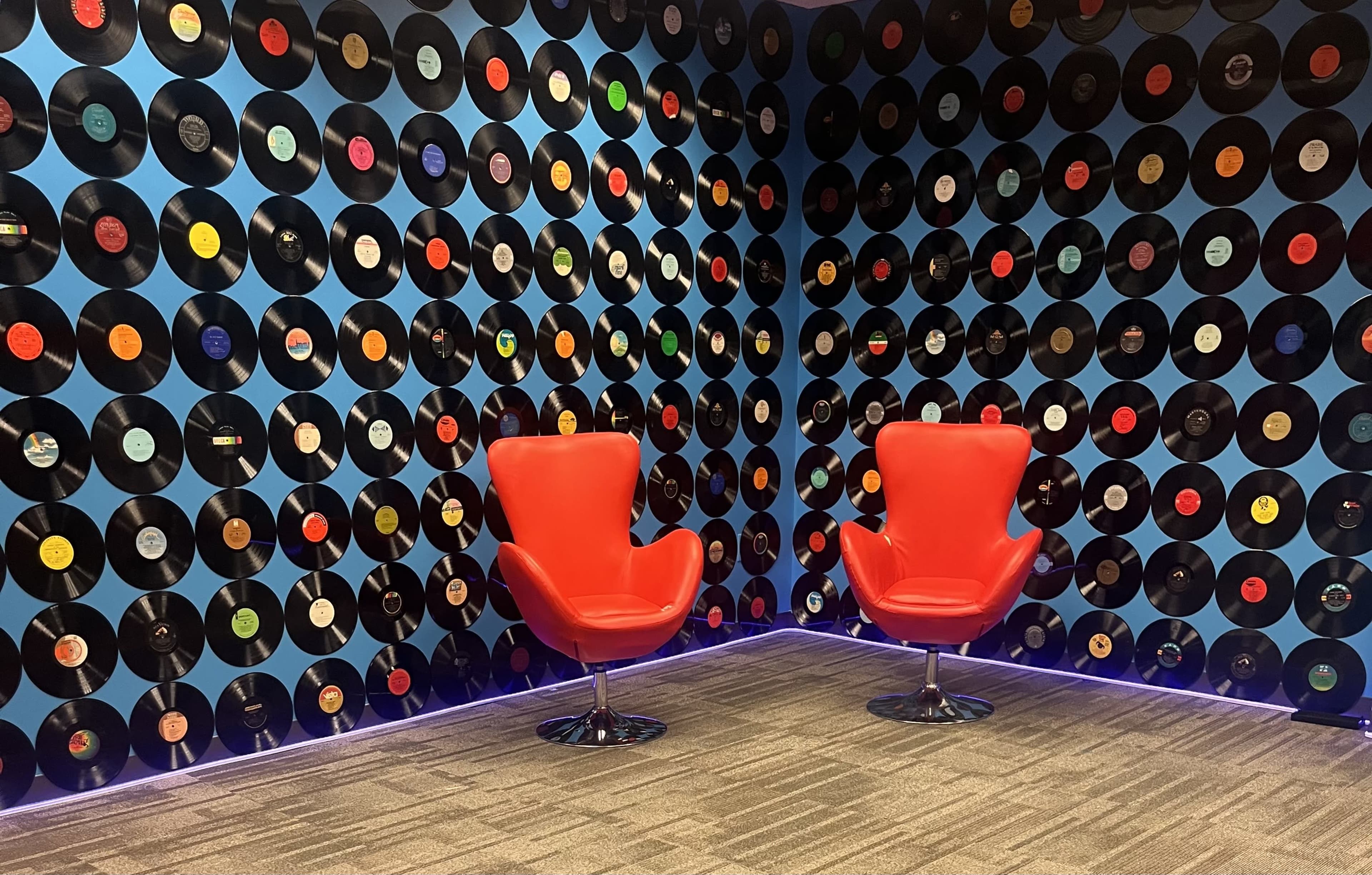 Two red chairs facing each other in a room with a wall covered in vinyl records.