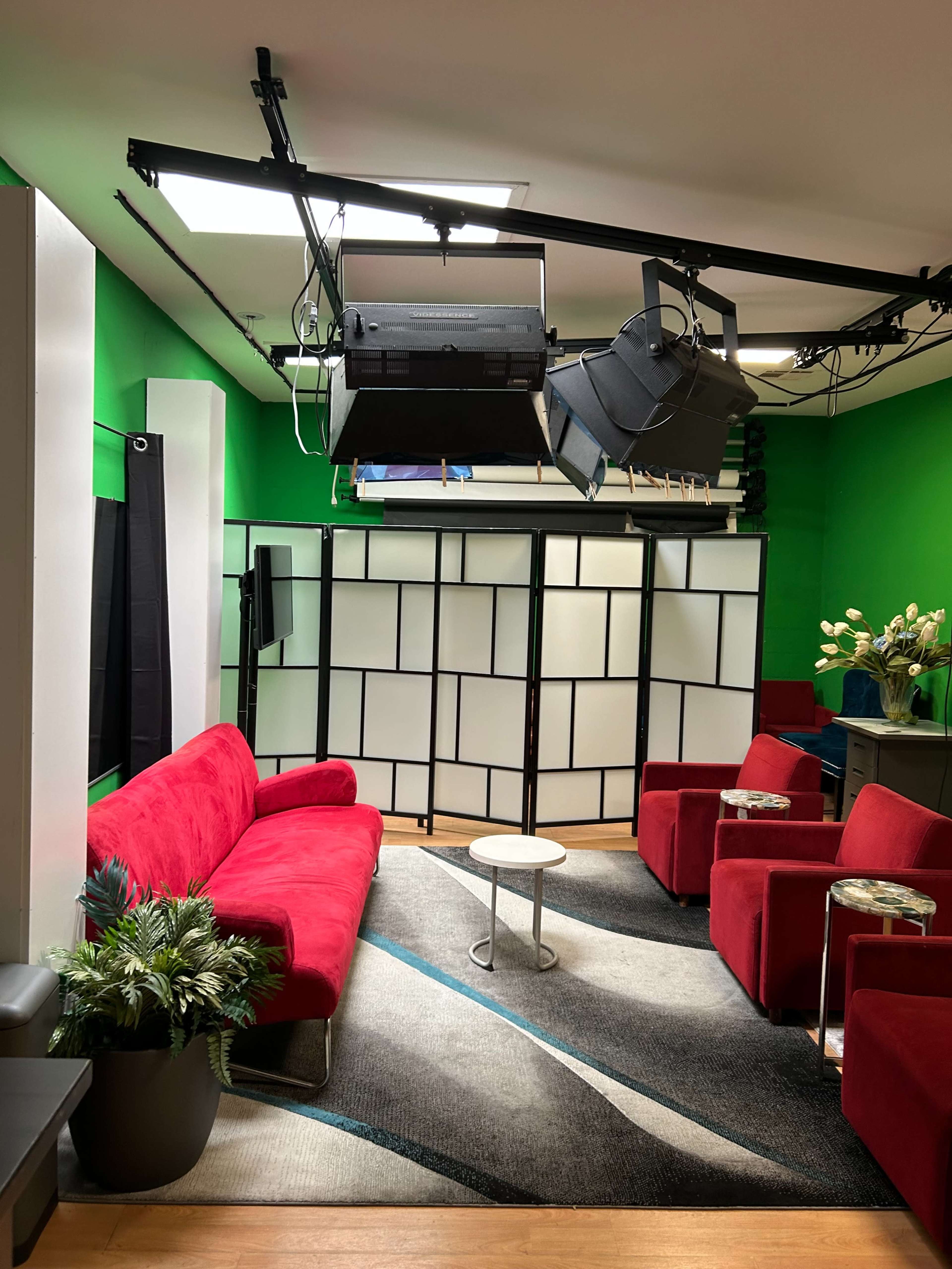 The image shows a television studio setup with red furniture, green walls, and a modern design.