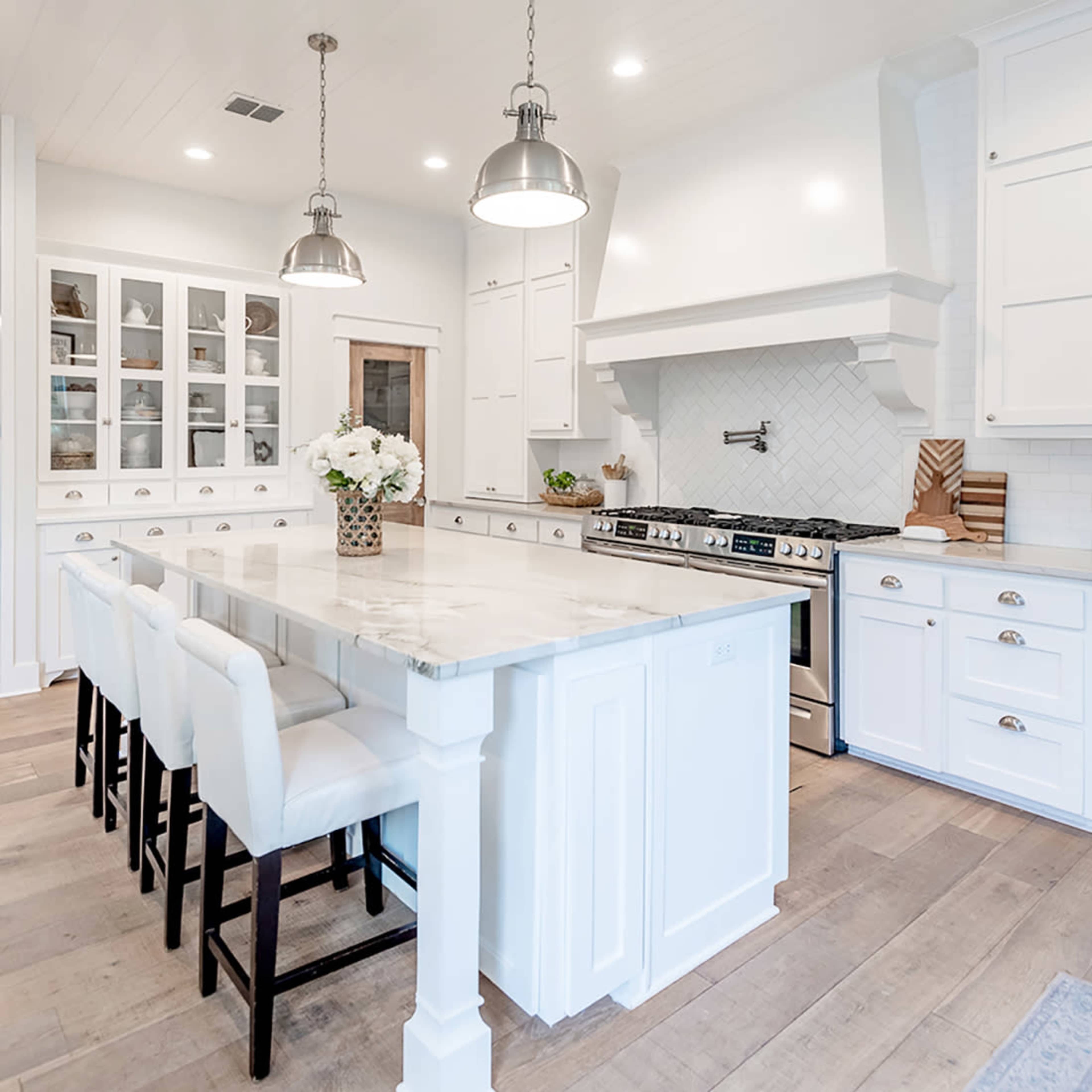 A modern kitchen with white cabinetry, a large marble island with seating for six, and stainless steel appliances.