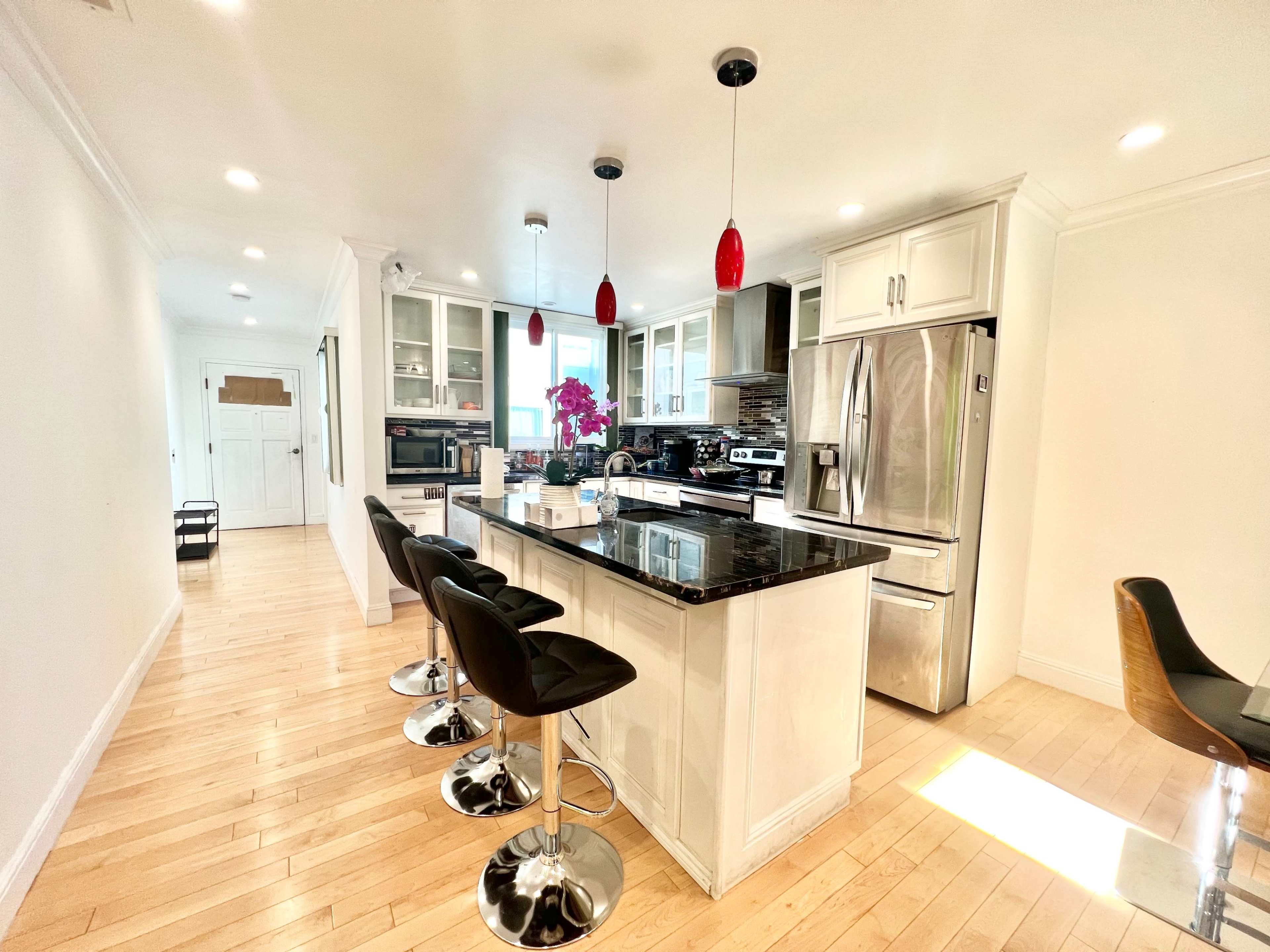 A modern kitchen featuring a central island with black bar stools, stainless steel appliances, and white cabinetry.
