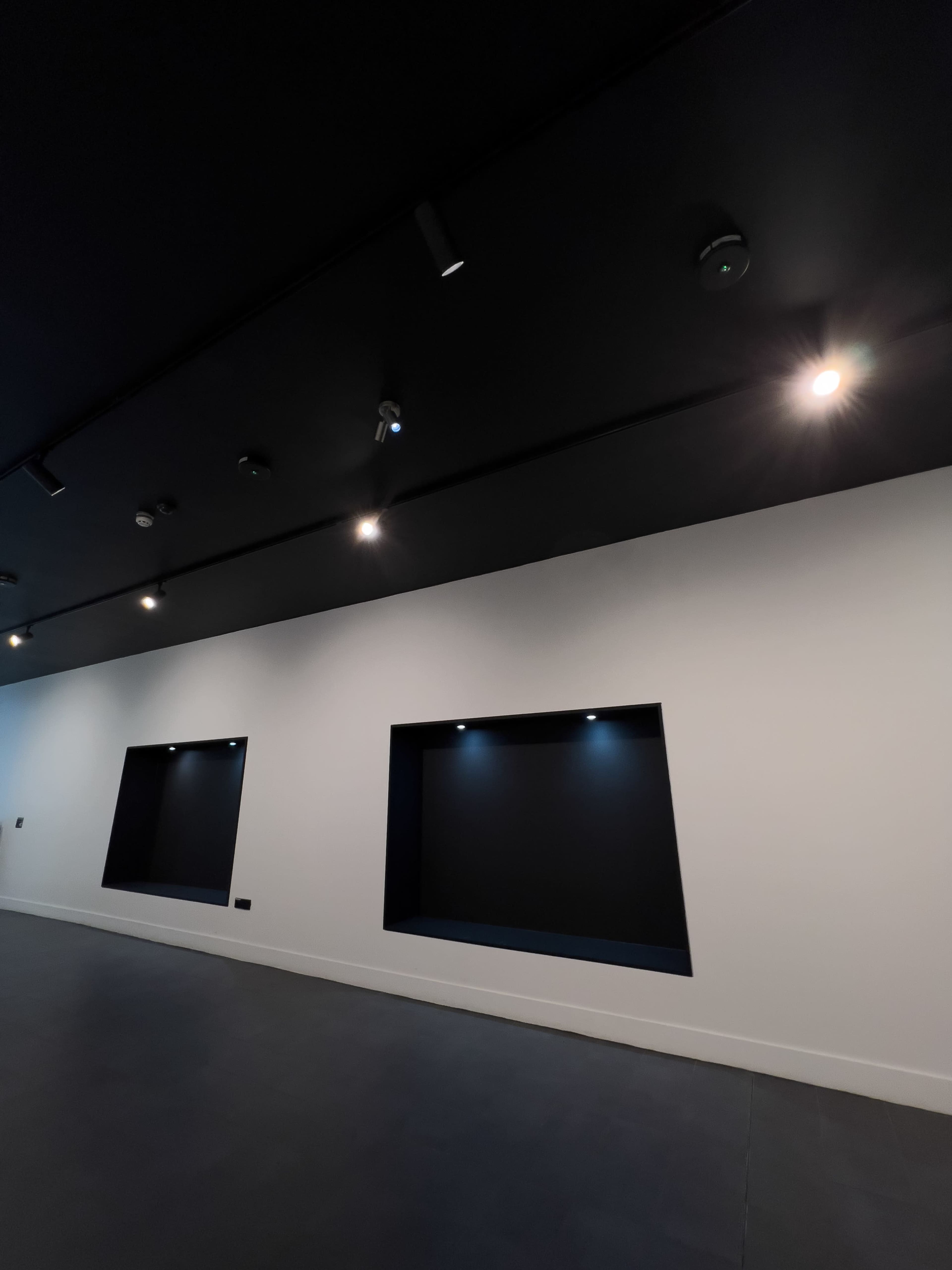 The image shows a room with black ceiling lights and two recessed wall niches on a white wall.