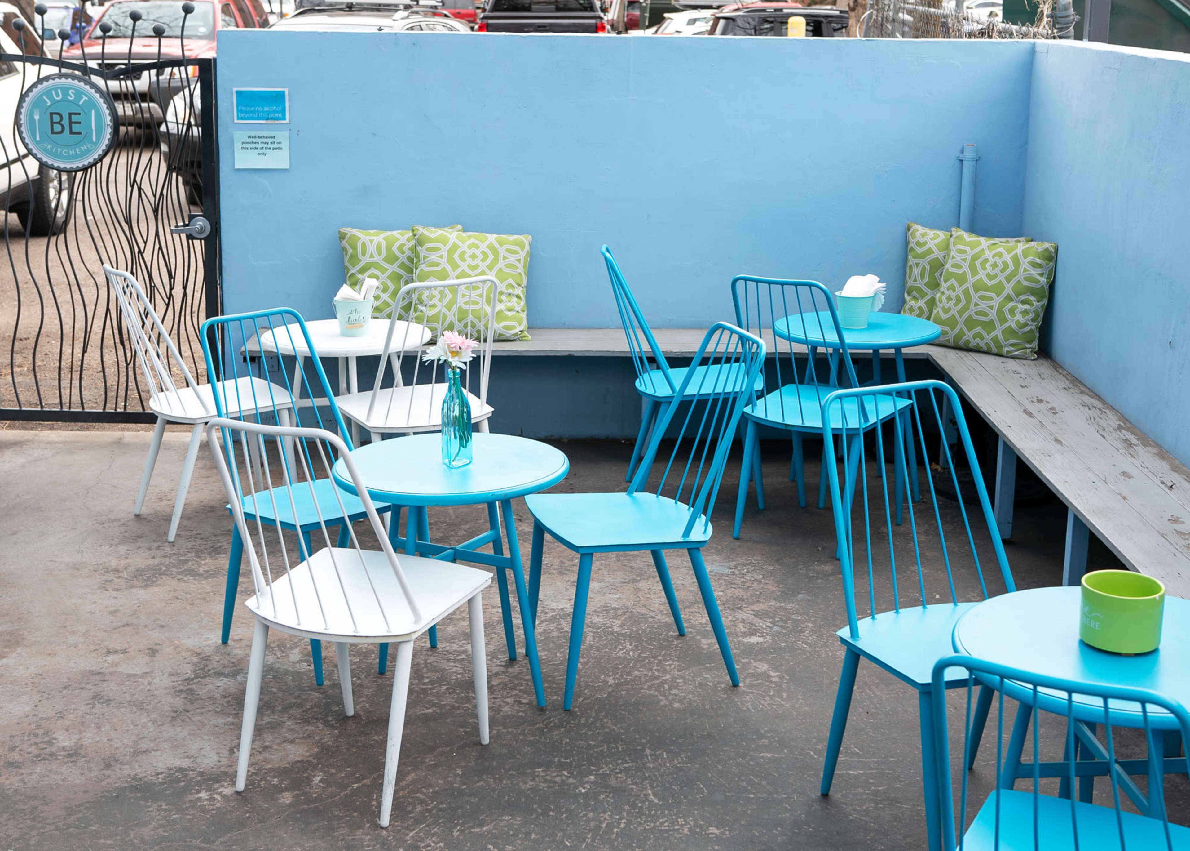 A small outdoor seating area features turquoise metal chairs and tables, with green decorative pillows on a bench against a blue wall.