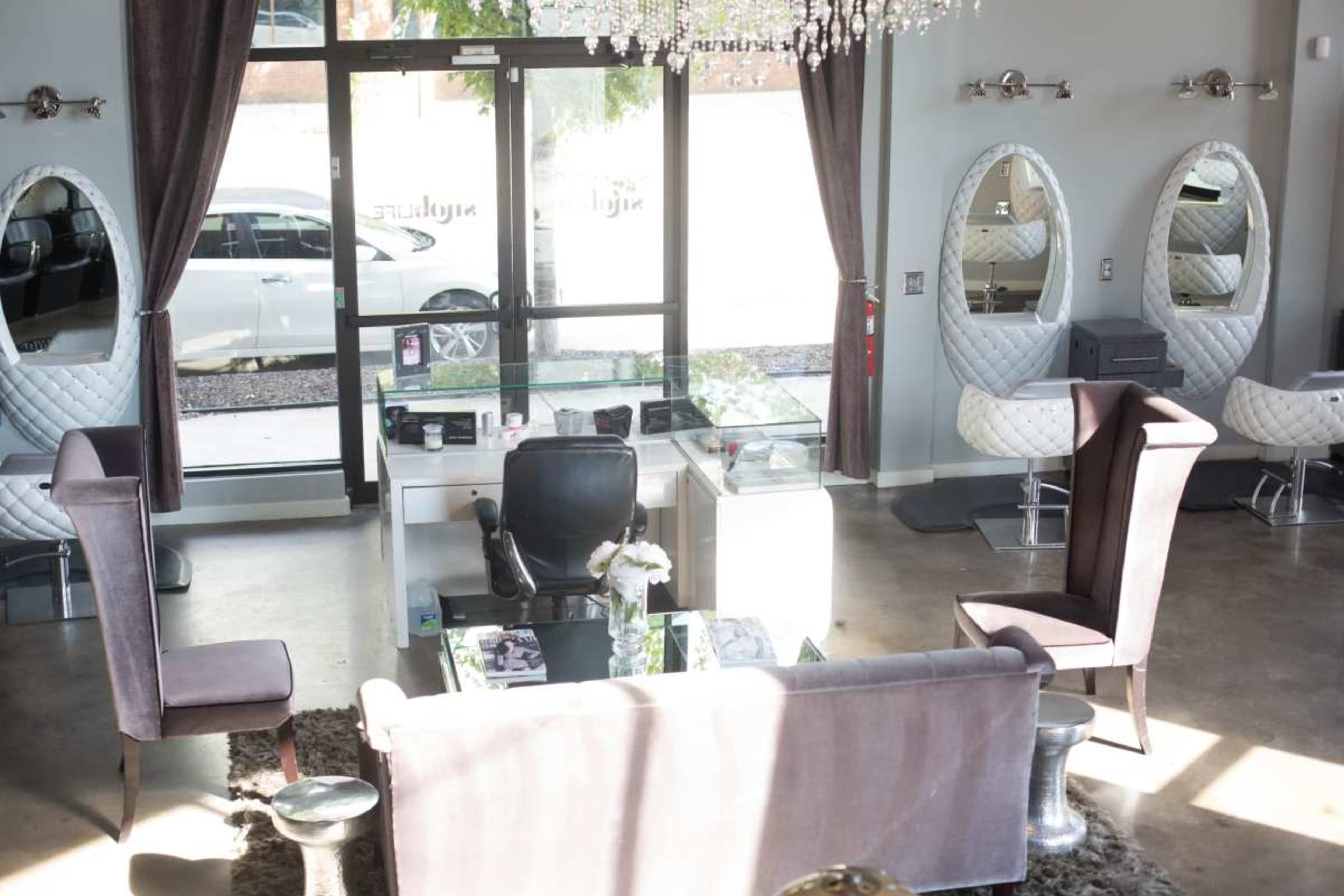 The image shows a stylish salon interior with plush seating, elegant mirrors, and a reception area featuring a glass display.