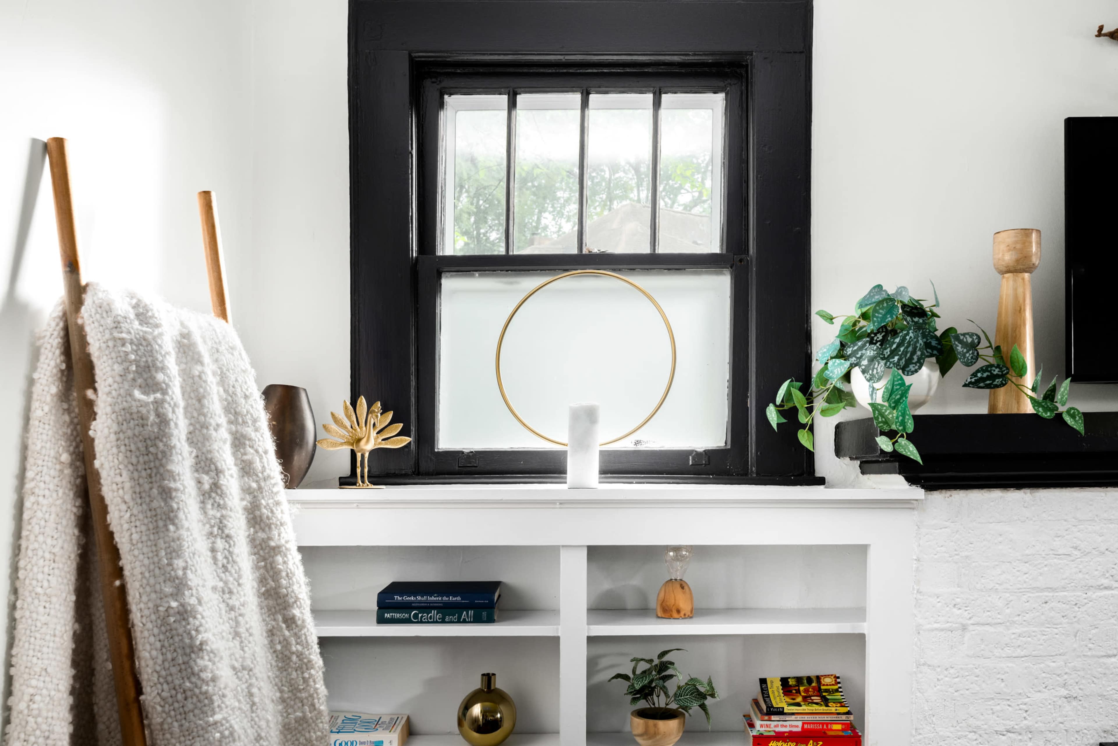 A cozy interior scene features a window with a gold circular decoration, surrounded by plants and decorative items on a white shelf.