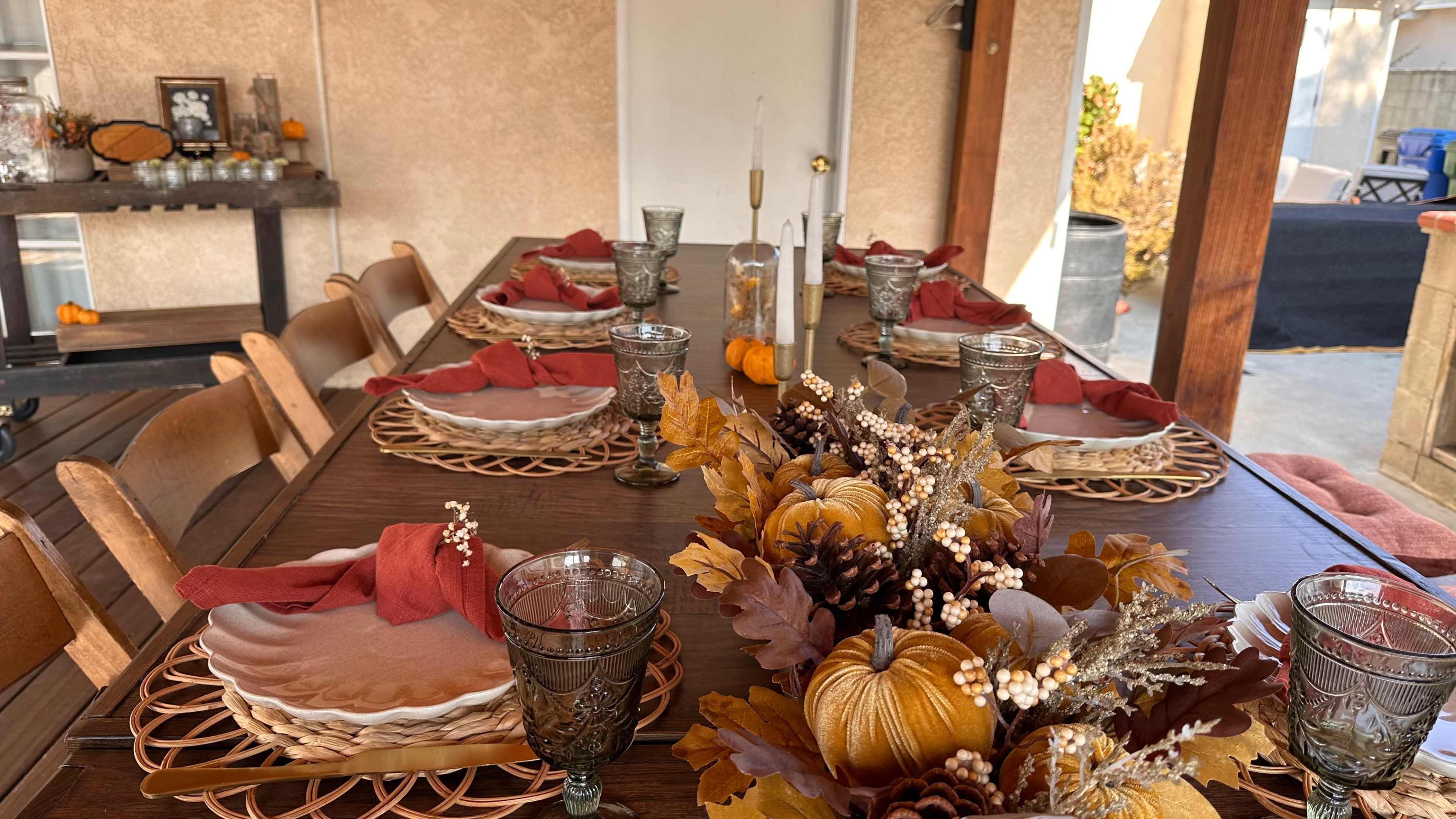 A long dining table is set with plates, glasses, and decorative autumn centerpieces featuring pumpkins and foliage.