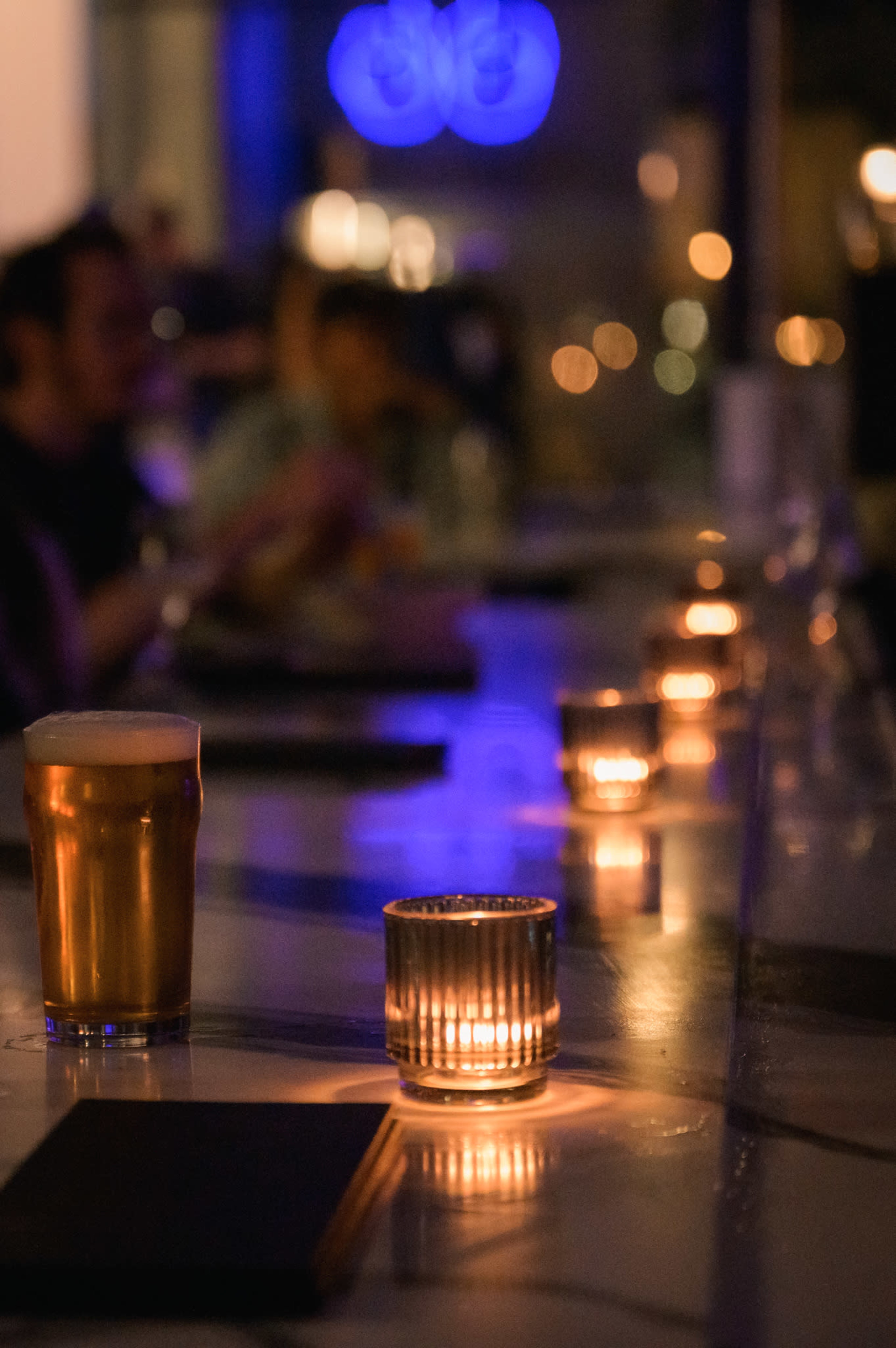 A dimly lit bar scene features a pint of beer and several flickering candles on a countertop.