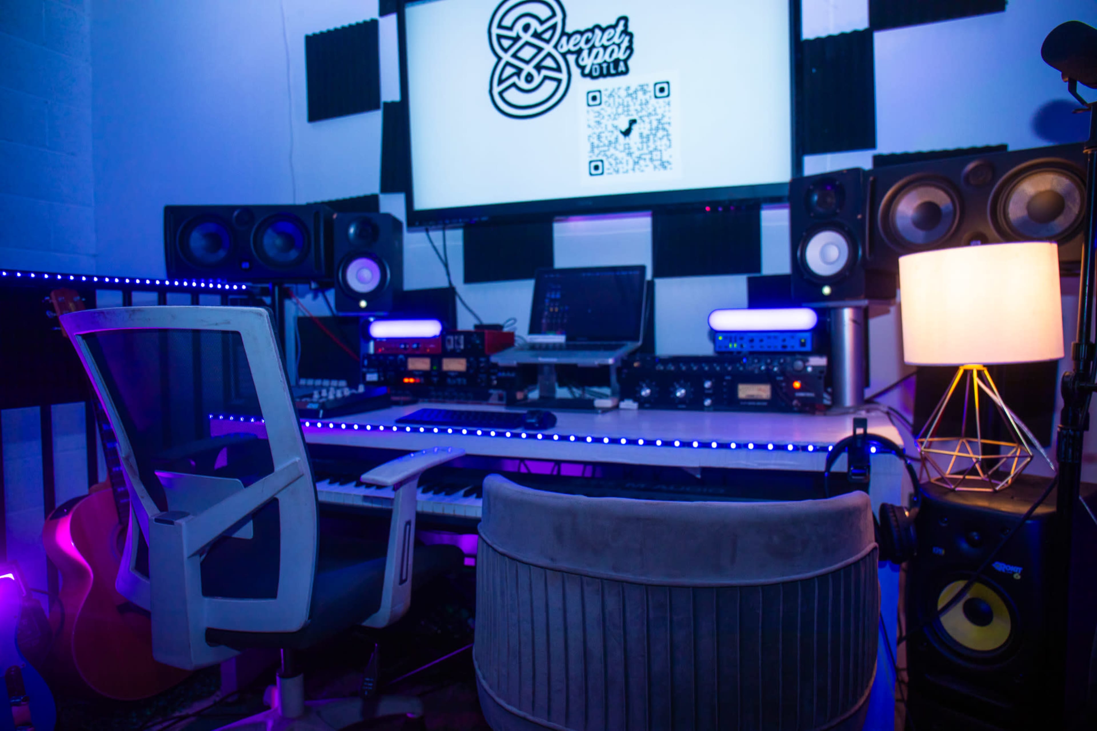 The image shows a modern music production studio equipped with various audio equipment, a keyboard, monitors, and ambient lighting.