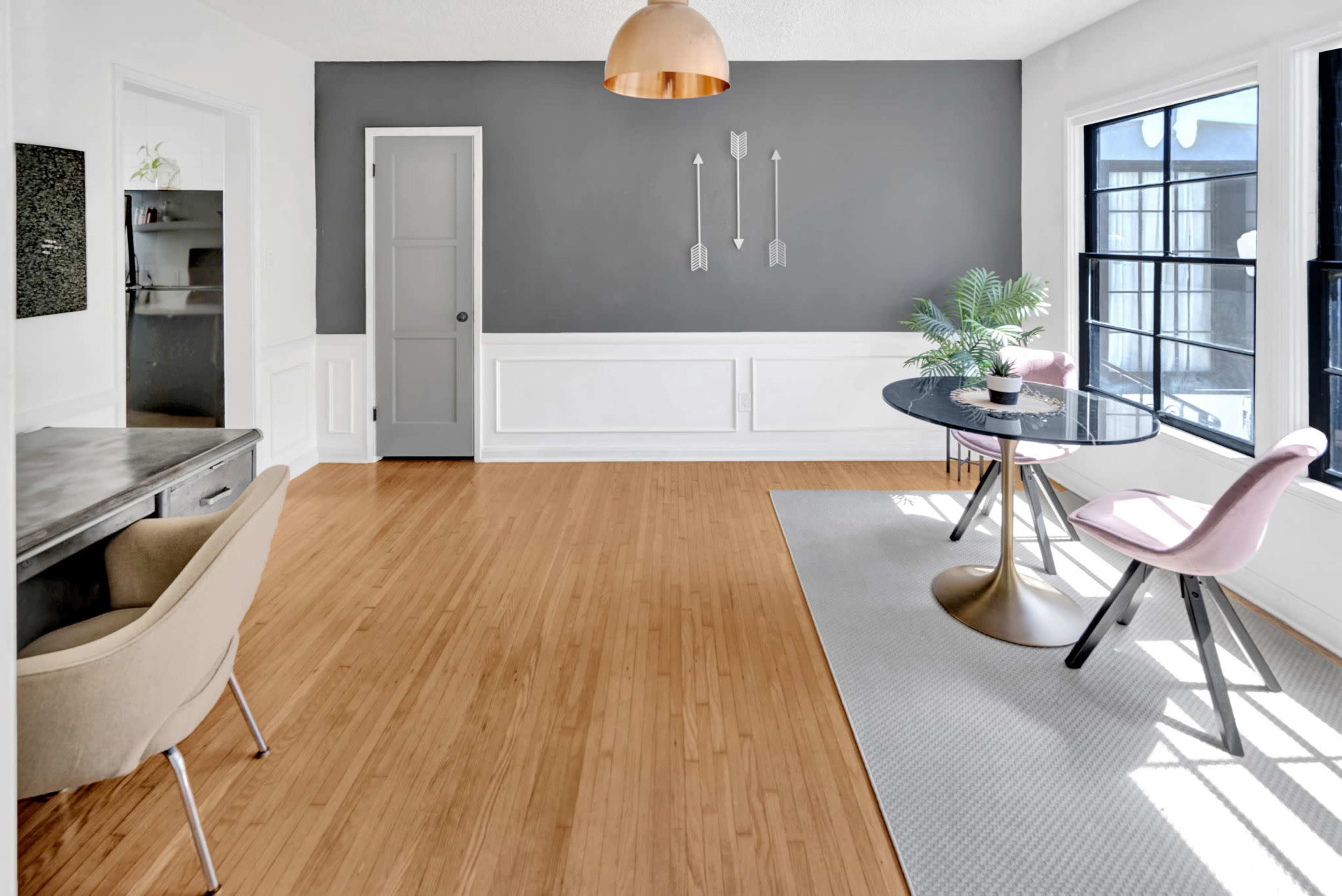 A modern dining area features a round black table with pink chairs, a gray accent wall, and bamboo flooring.
