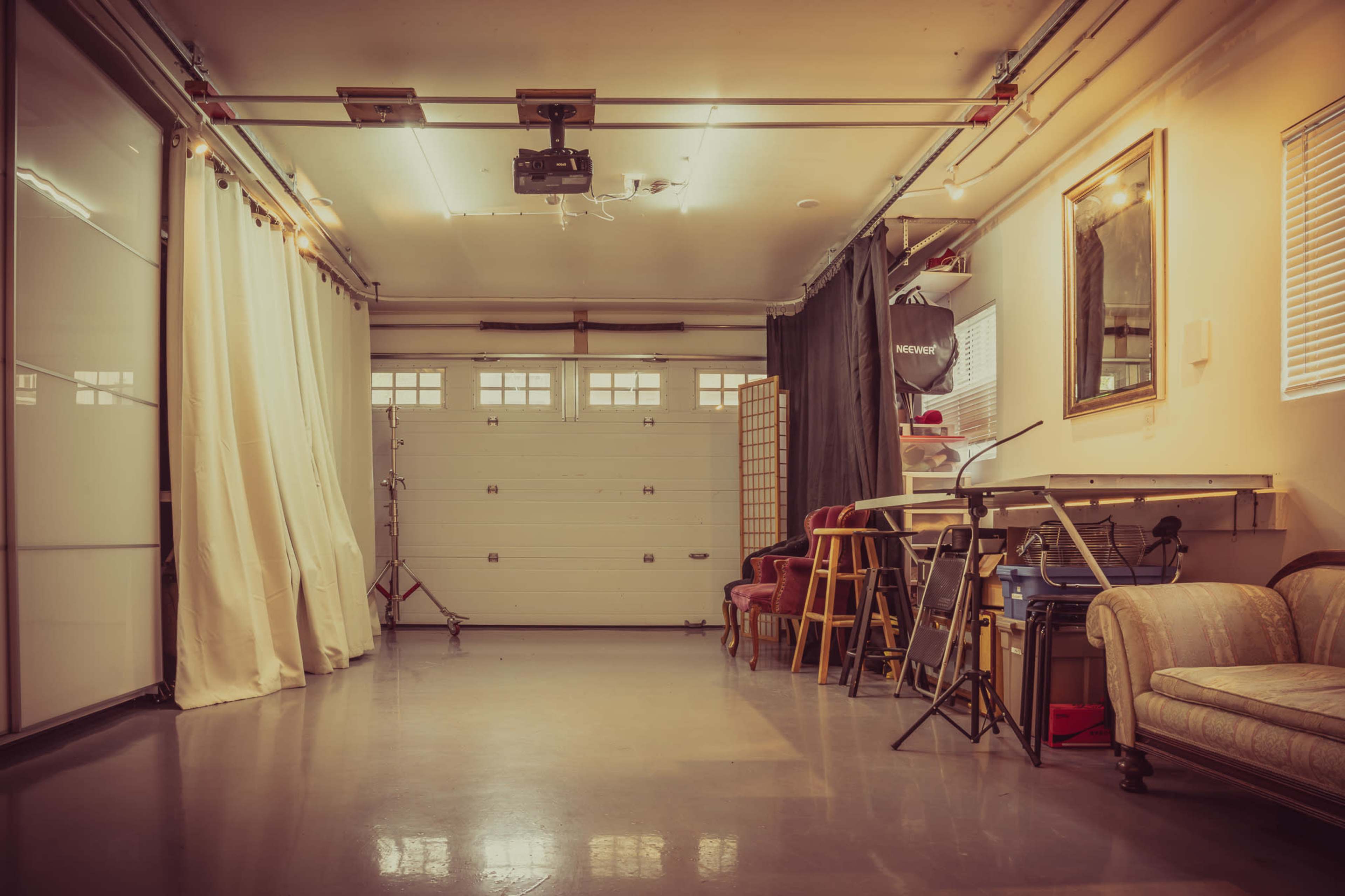 A spacious, well-lit studio with a garage door, various seating options, and equipment for photography or videography.