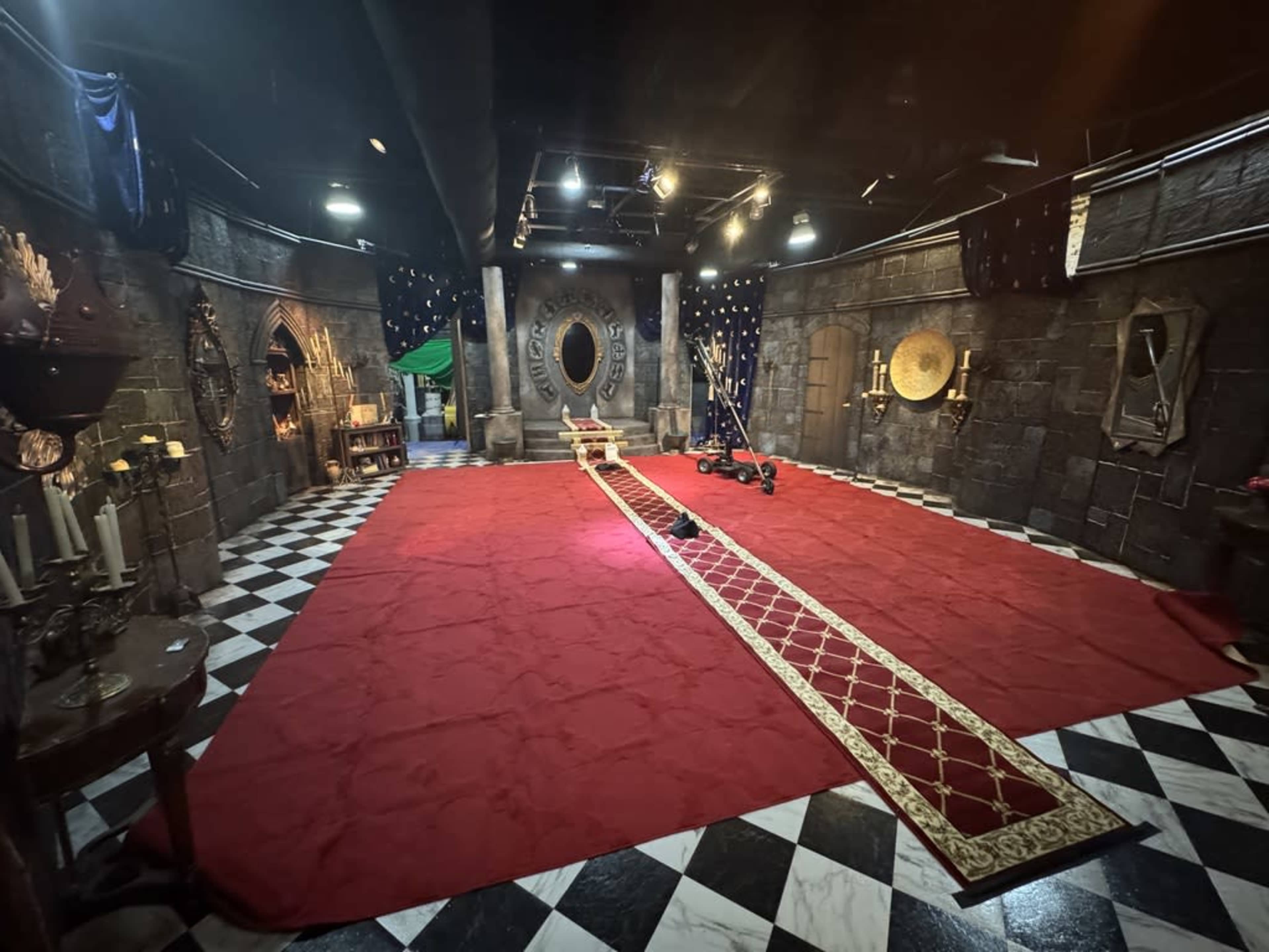The image shows a dimly lit room with black and white checkered flooring, adorned with stone-like walls, featuring a red carpet running down the center and decorative mirrors and candles along the sides.