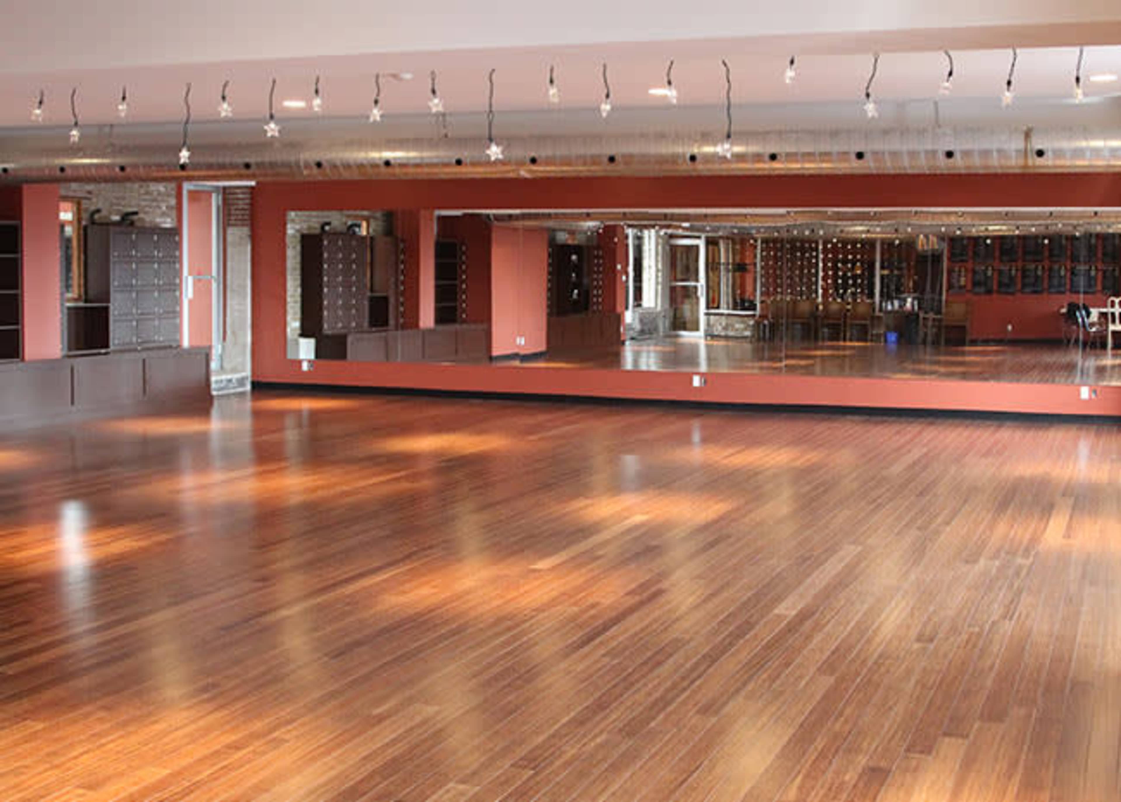 The image shows a spacious room with hardwood floors and large mirrors along one wall, suitable for dance or exercise activities.