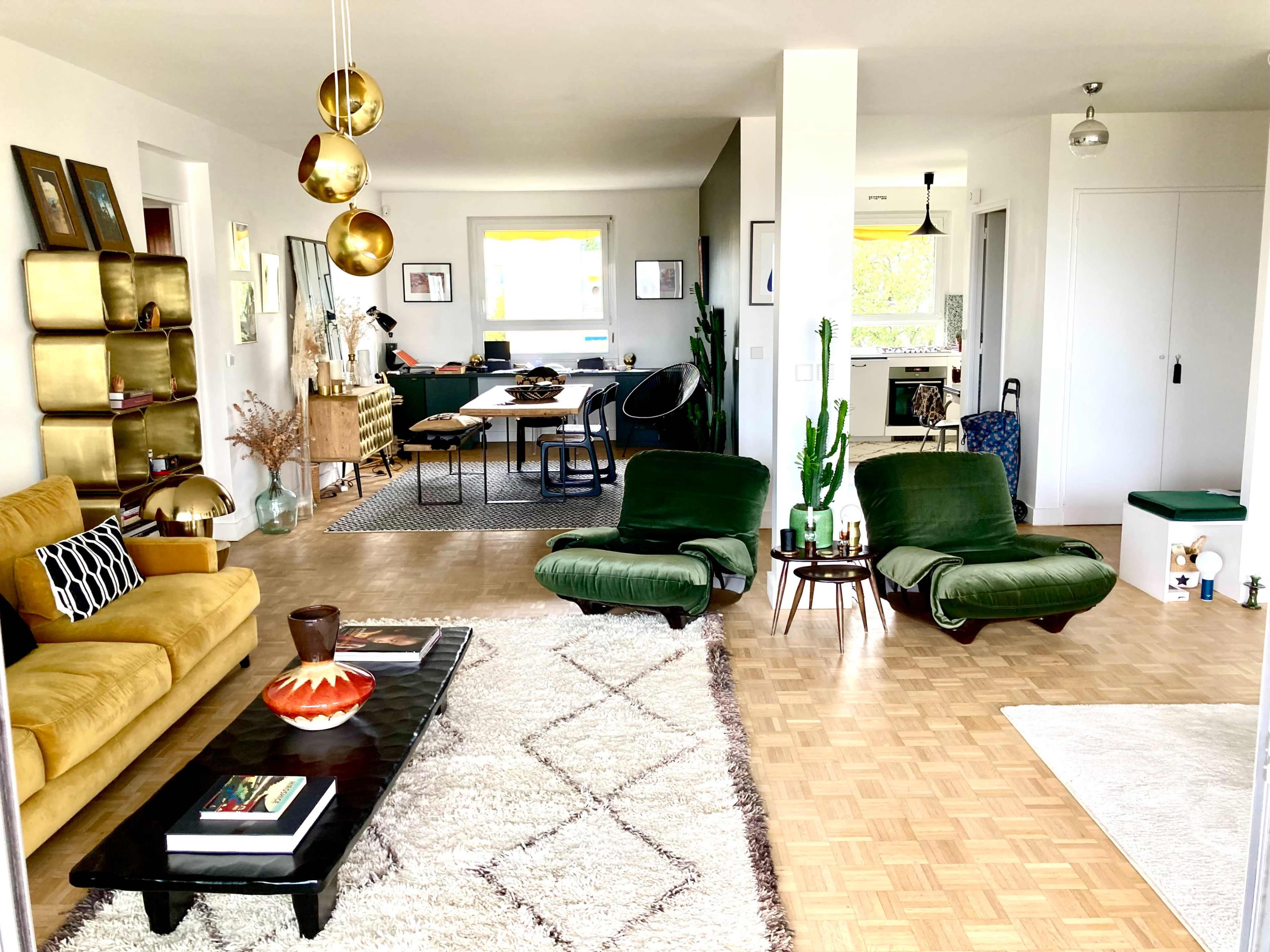 A modern living room featuring two green lounge chairs, a coffee table, a large area rug, and a dining area in the background.