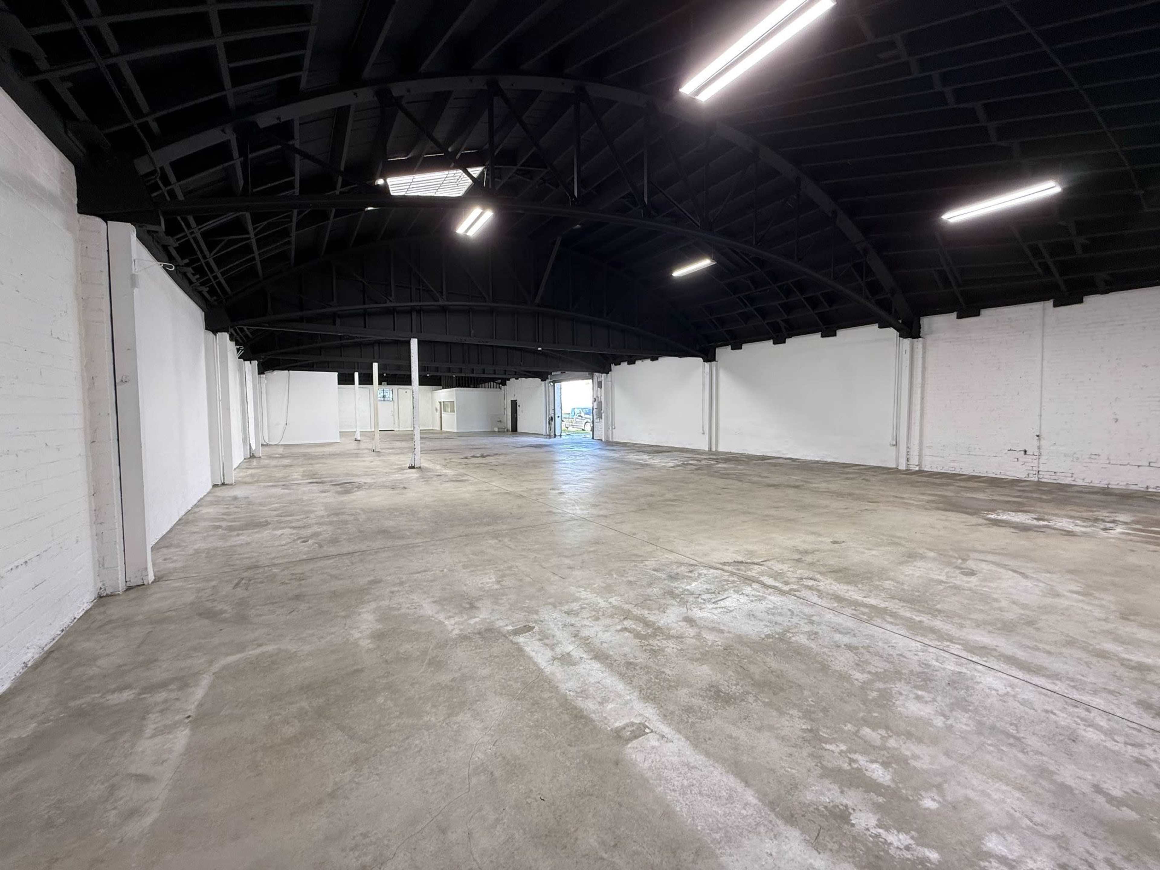 The image shows a large, empty commercial space with a polished concrete floor and a curved black ceiling.