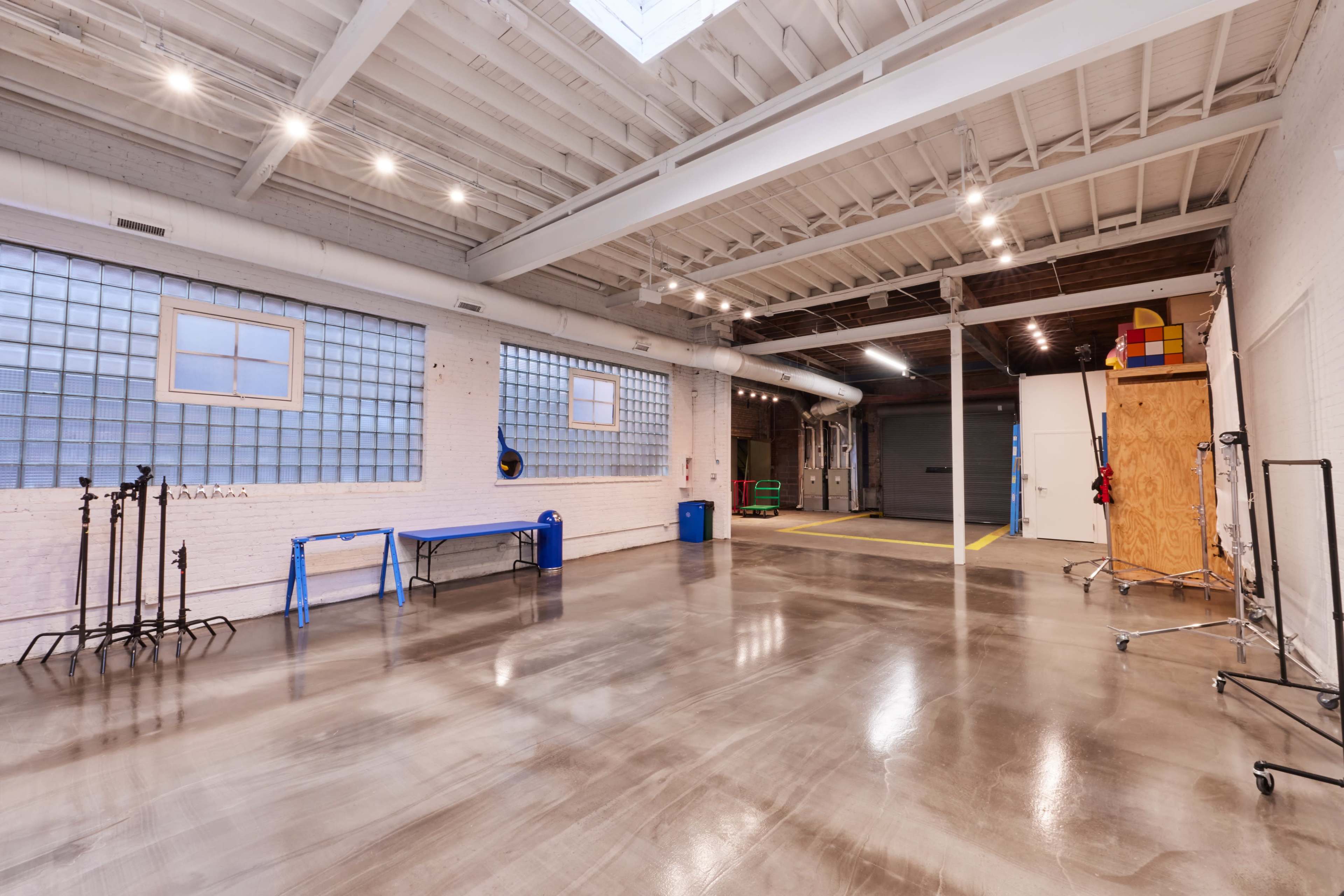A spacious and well-lit industrial interior with polished concrete floors, large windows, and various equipment arranged along the walls.