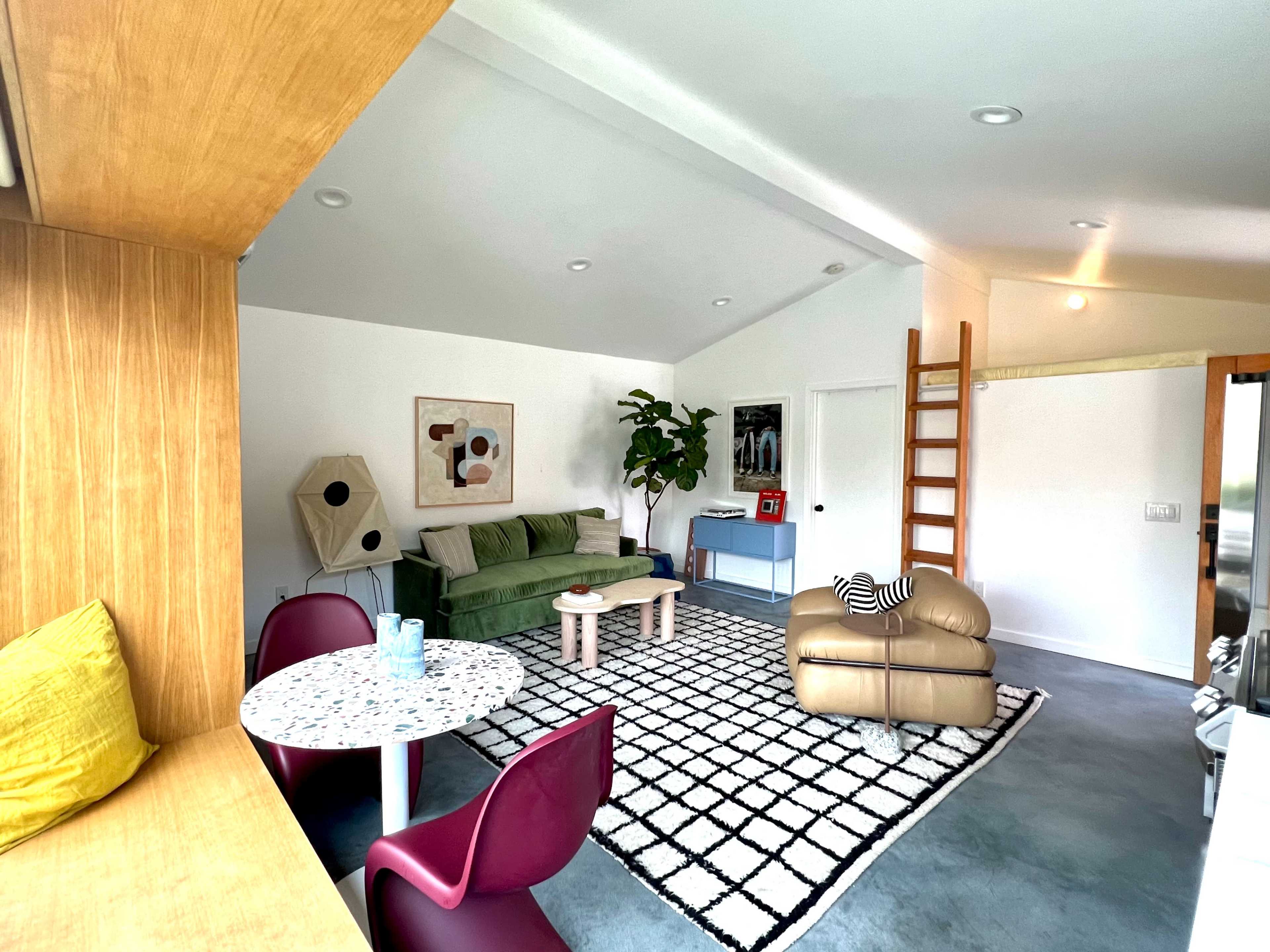 A modern, open living space with a green sofa, a round dining table, and a ladder leading to a loft area.