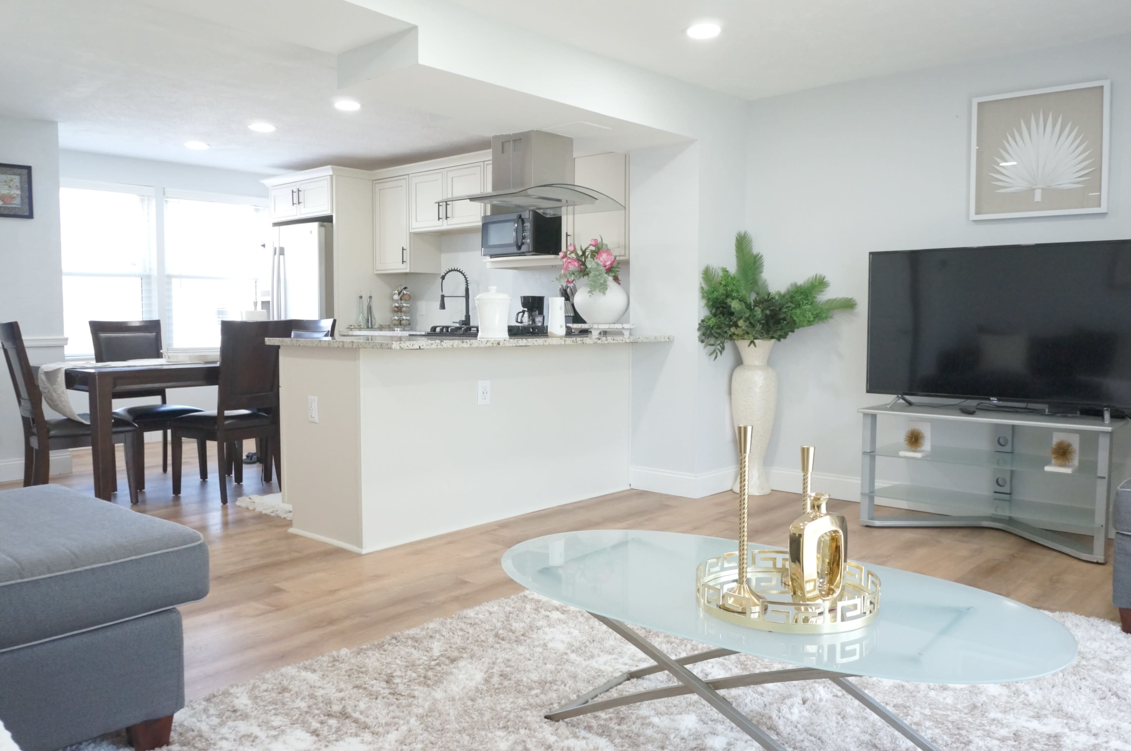 The image shows a modern, light-filled living area with an open kitchen, featuring a cozy seating arrangement and a stylish coffee table.