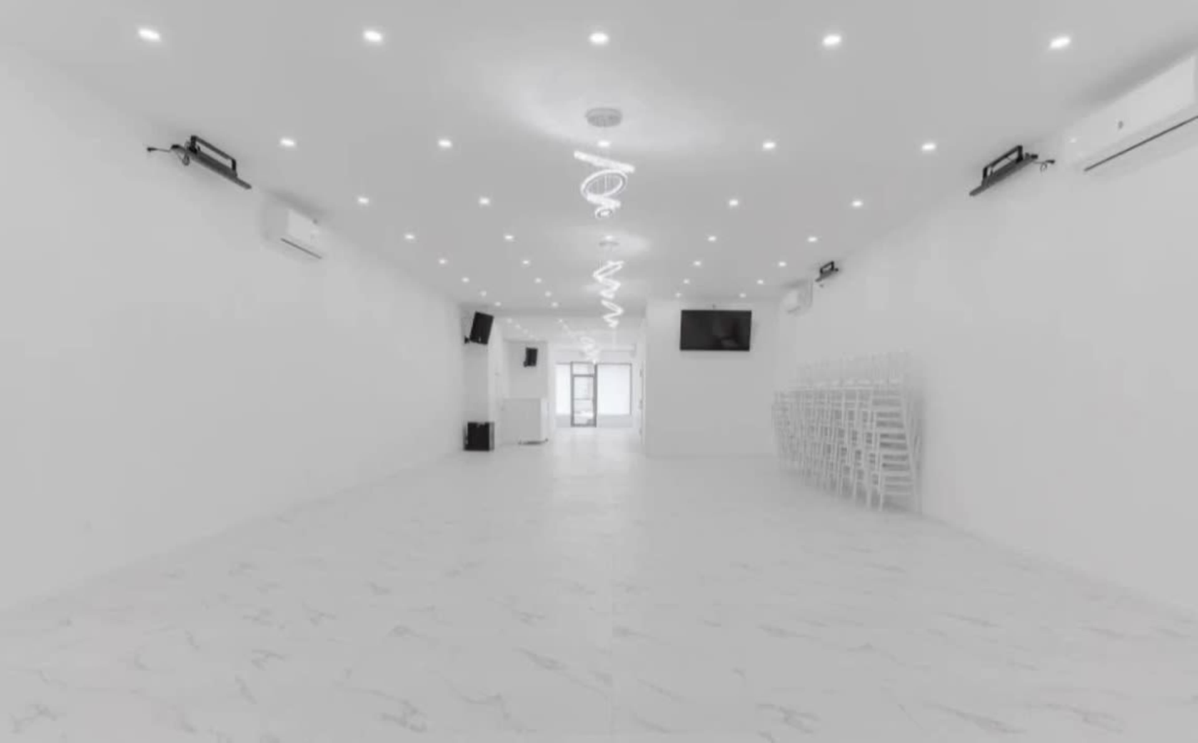 The image shows a spacious, empty room with white walls and ceiling, equipped with air conditioning units and minimalist lighting.