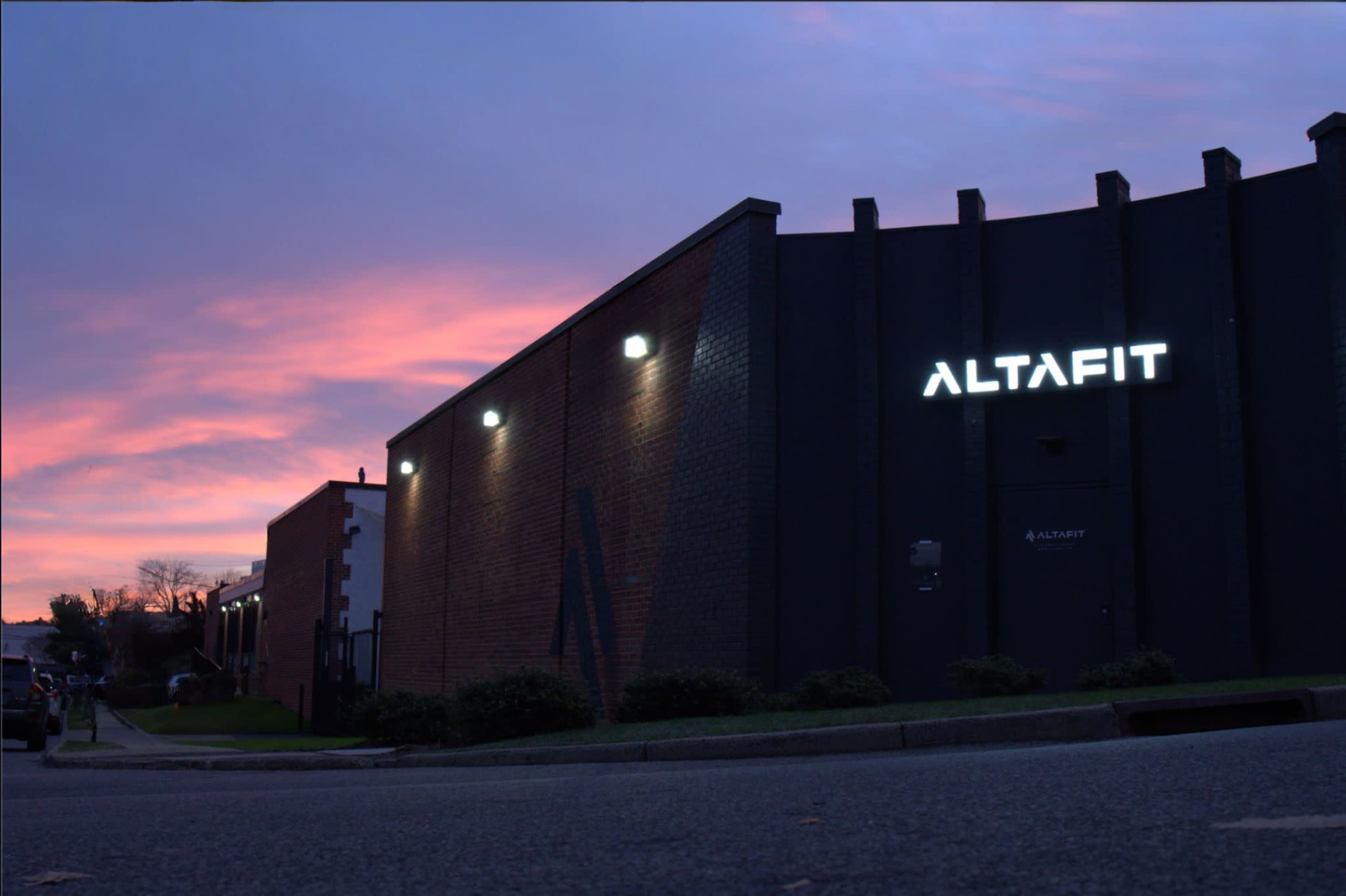 A building with a prominent "ALTAFIT" sign illuminated against a colorful sunset sky.