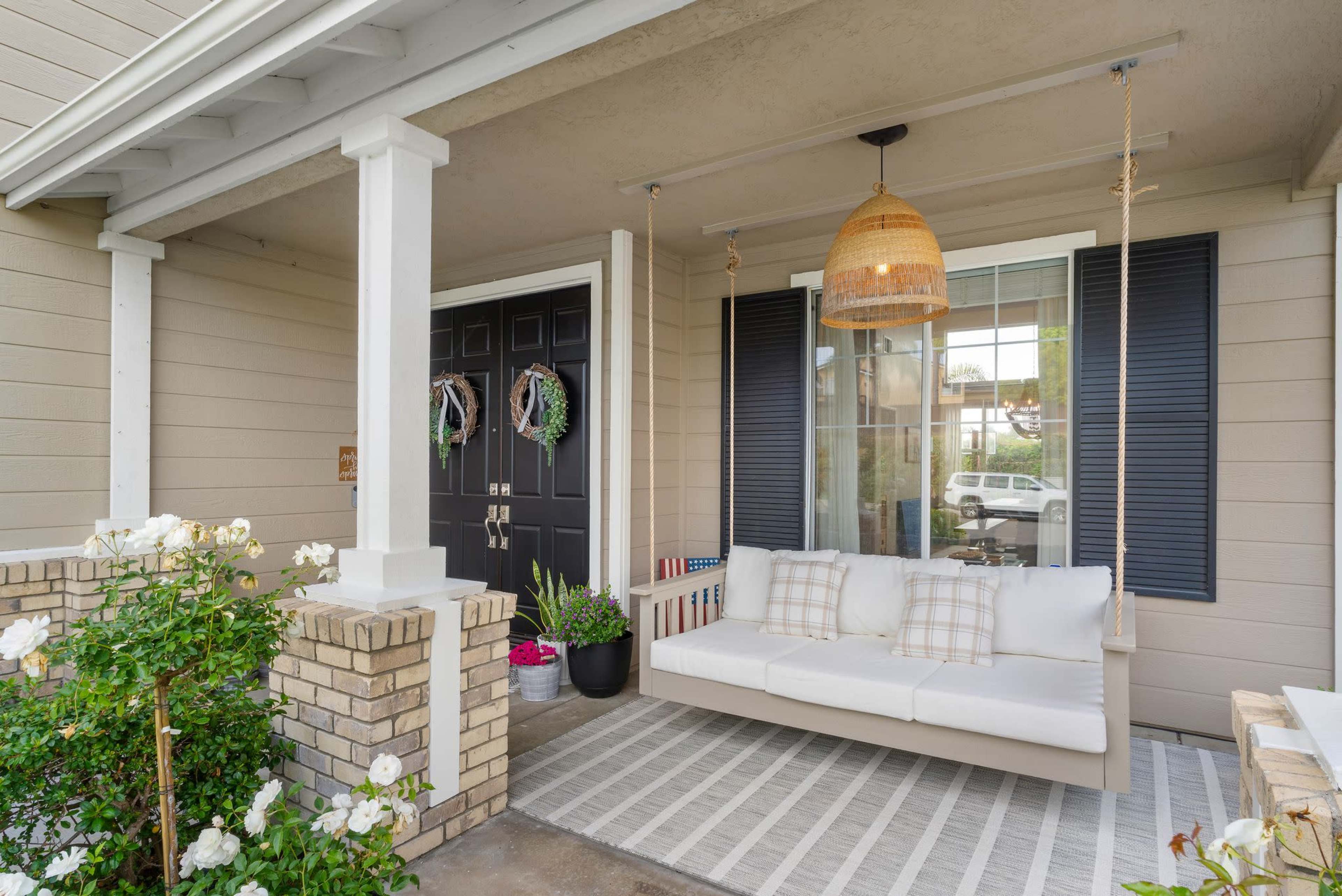 A front porch featuring a white swing bed, potted plants, and decorative wreaths on the double doors.